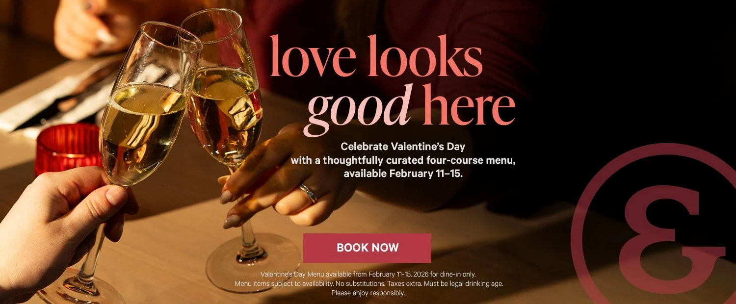Two people clinking glasses of white wine, celebrating Valentine’s Day at a restaurant with a dimly lit, romantic ambiance.