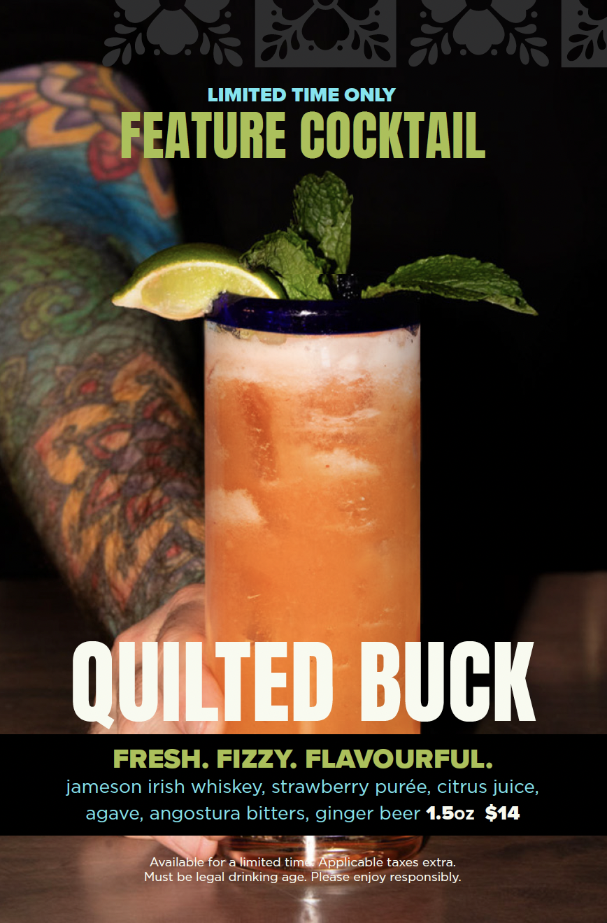 A colorful cocktail with a lime wedge and mint leaves garnished on top, served in a tall glass filled with ice. The background is dark with tattooed arm visible on the side.