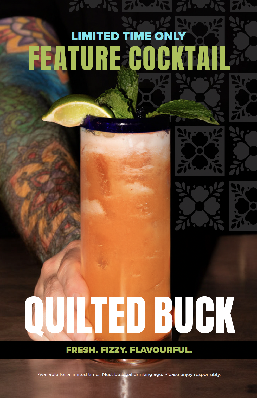 A colorful cocktail with lime wedge and mint garnish in a tall glass, held by a tattooed arm, with promotional text for a limited-time feature cocktail called 'Quilted Buck,' described as fresh, fizzy, and flavourful.