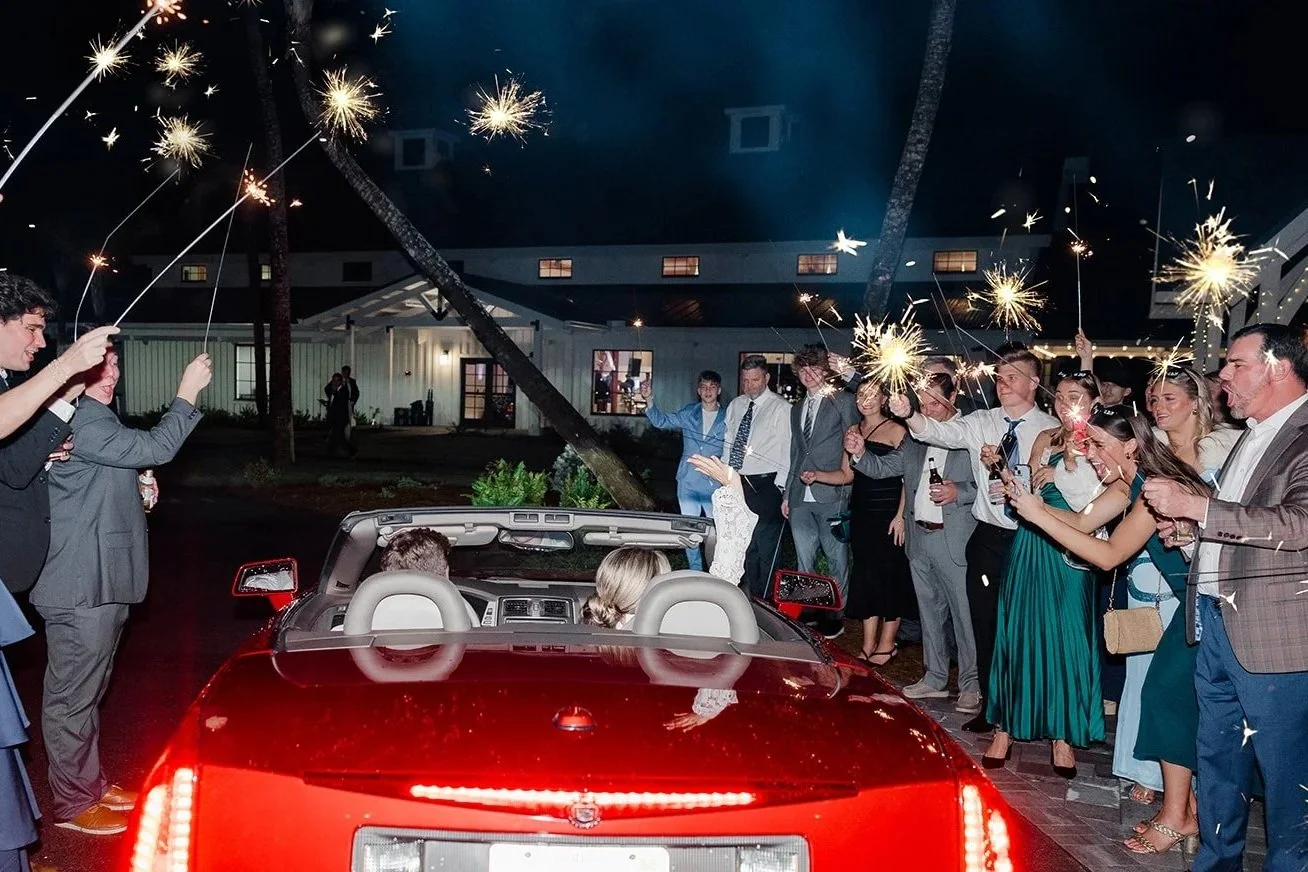 People celebrating with sparklers around a red convertible car at night.