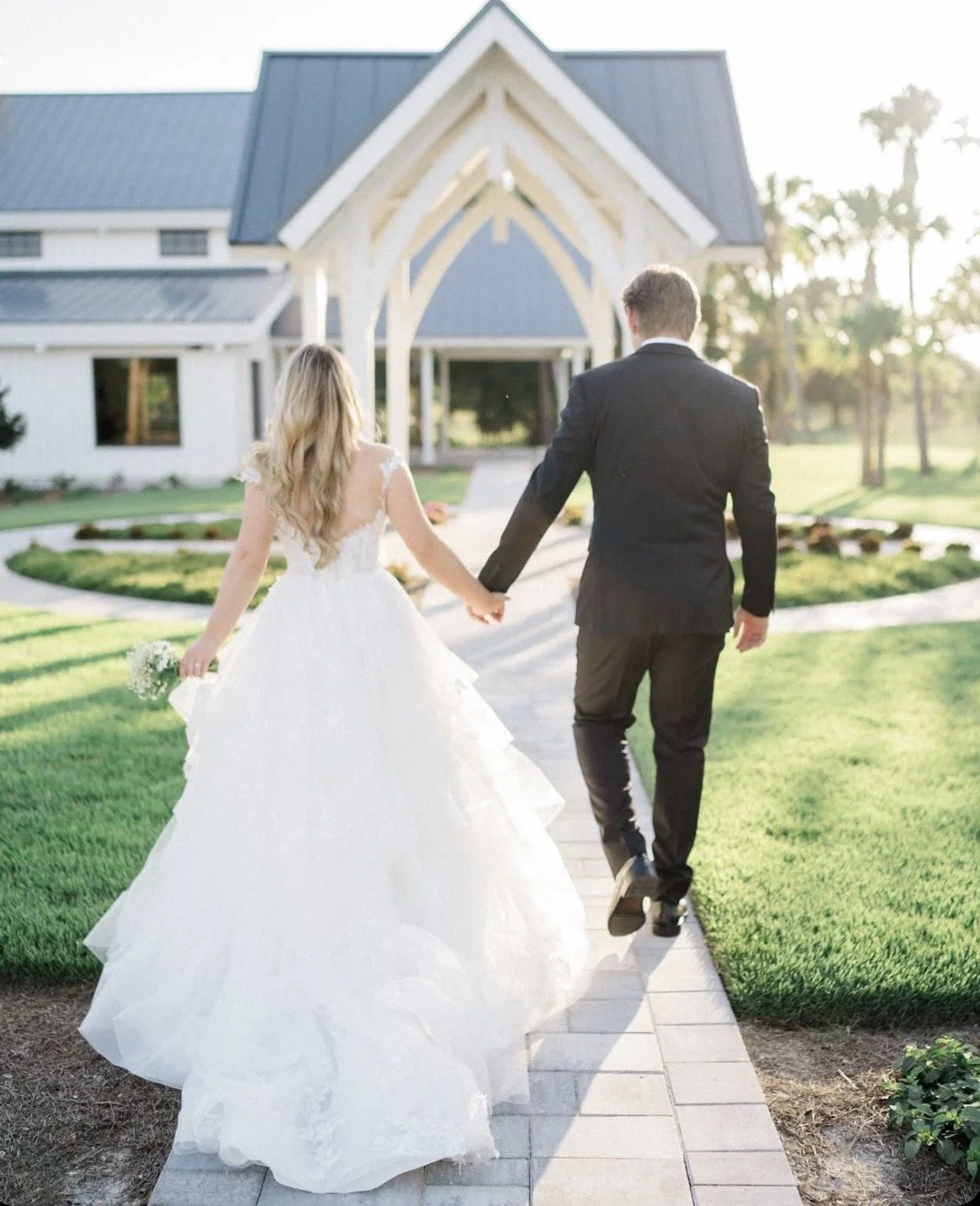 A bride and groom holding hands walking toward a church or wedding venue during daylight at Celebration Grove Wedding and Event Venue in Vero Beach.