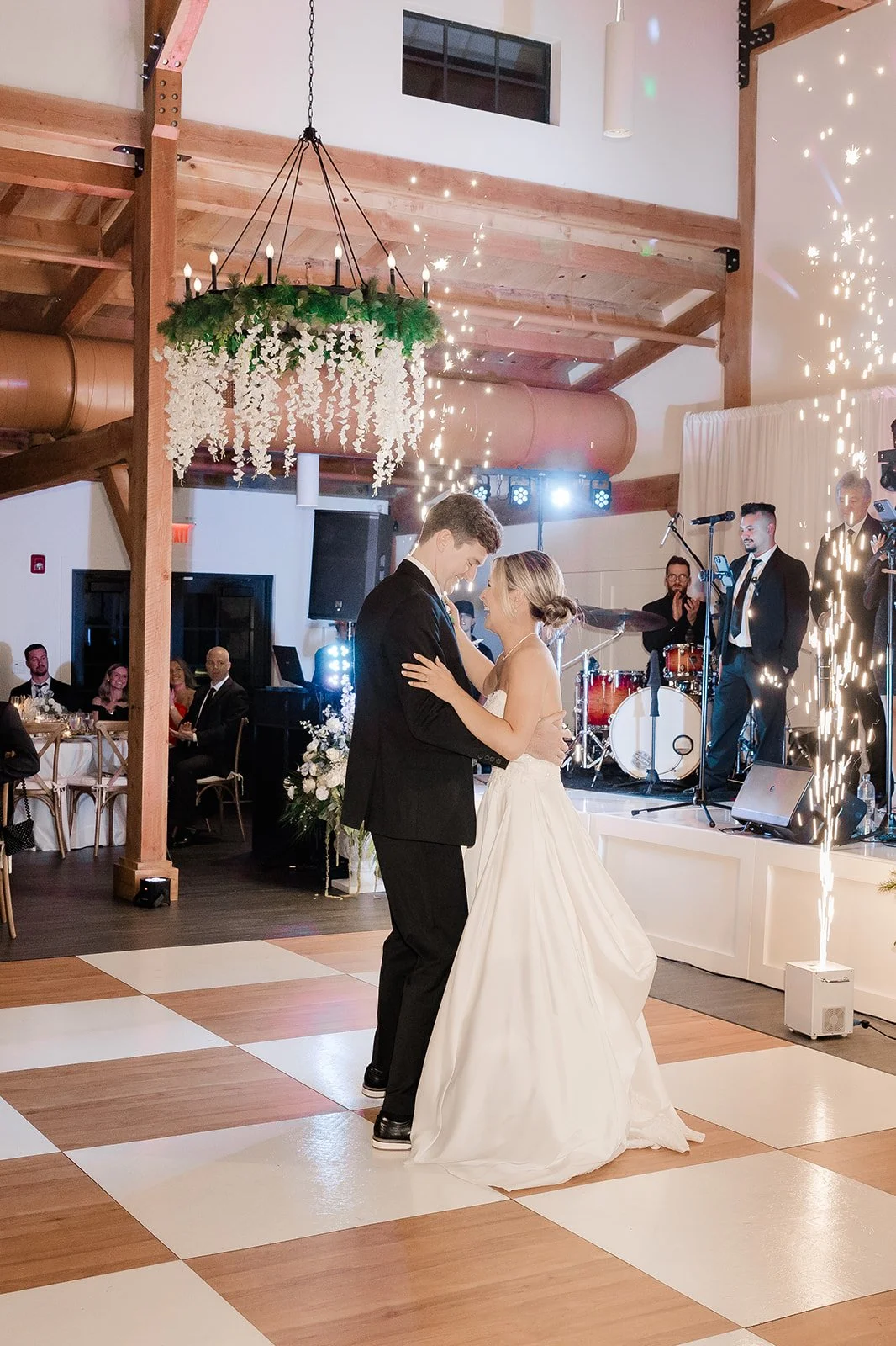 Bride and groom sharing their first dance at wedding reception with guests and band performing in background in the reception hall at Celebration Grove Wedding and Event Venue in Vero Beach.