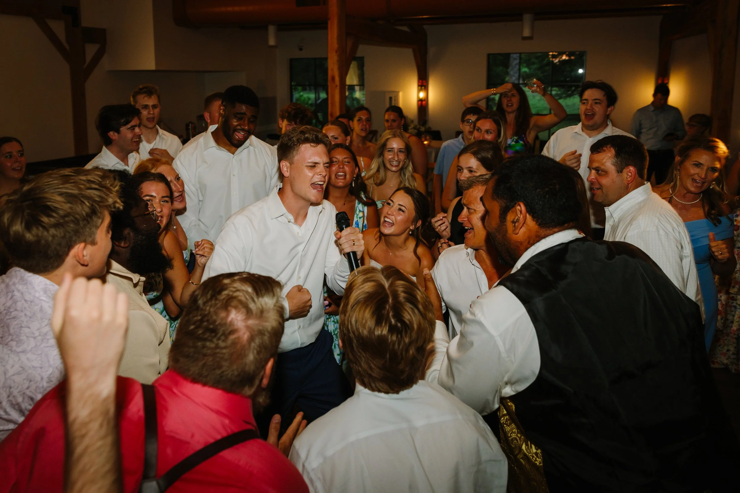 Group of people dancing and singing with a man holding a microphone at a lively gathering or party indoors.