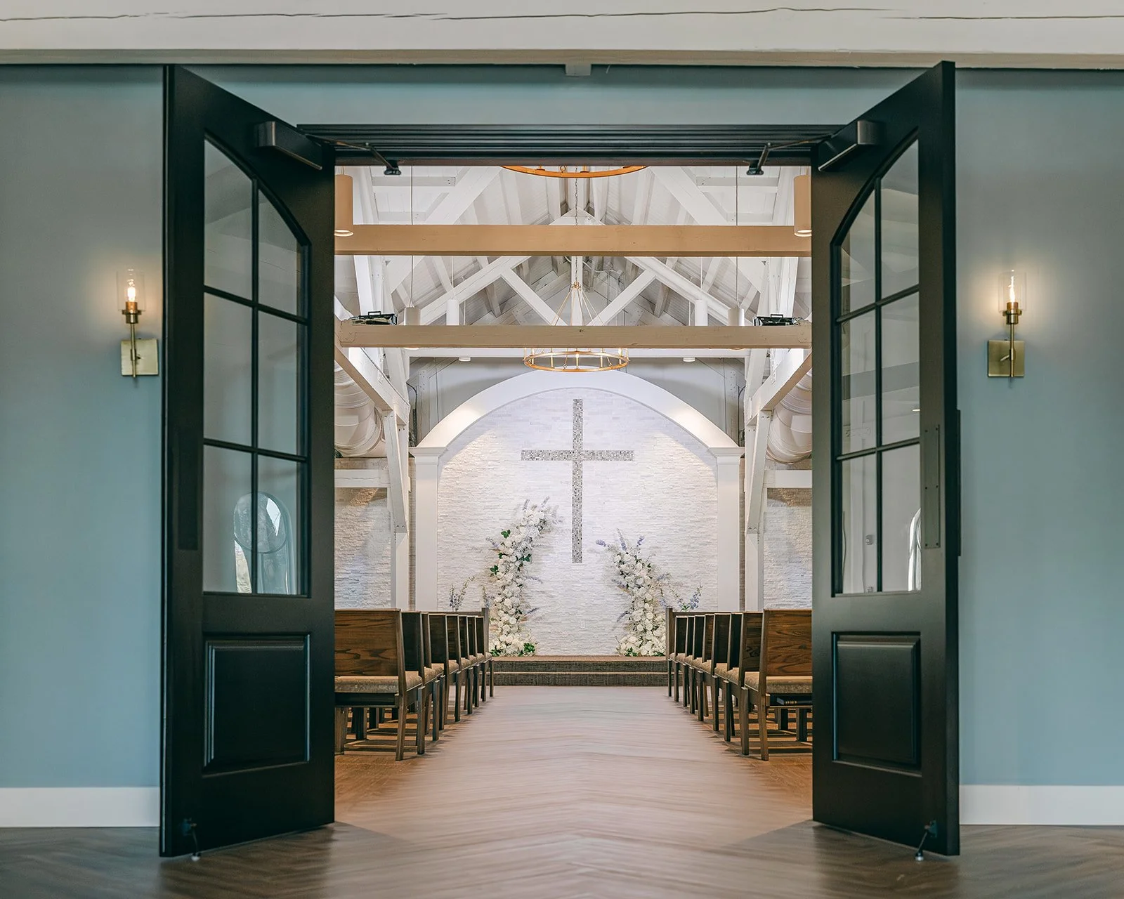 Interior view of Celebration Grove sanctuary in Vero Beach with grand doors opening to reveal the altar’s large cross beneath artisan post-and-beam architecture and elegant chandeliers.