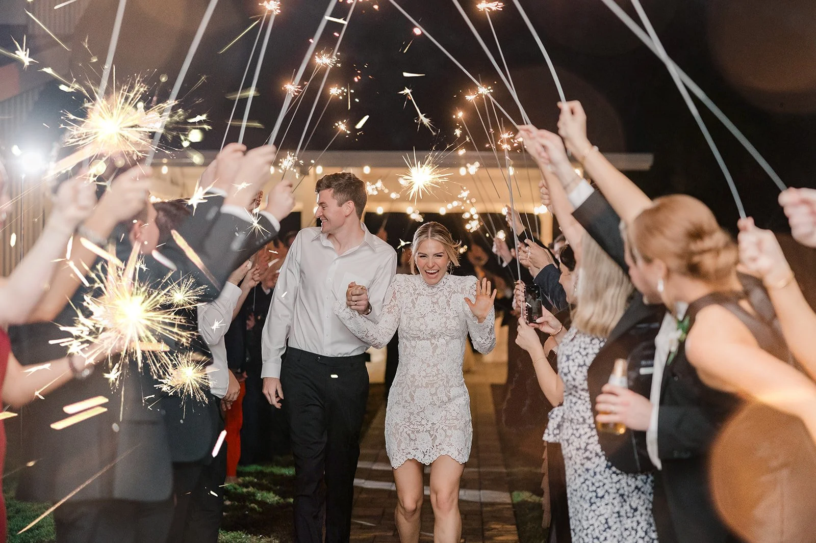 A bride and groom walking through a celebration with sparklers held by guests at night.
