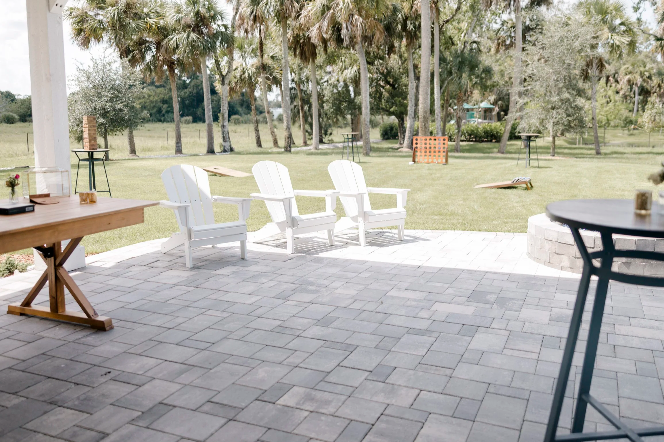 Charming covered veranda at Celebration Grove with Adirondack chairs, firepit, and garden string lights, ideal for cocktail hour and open-air mingling during weddings and events in Vero Beach.