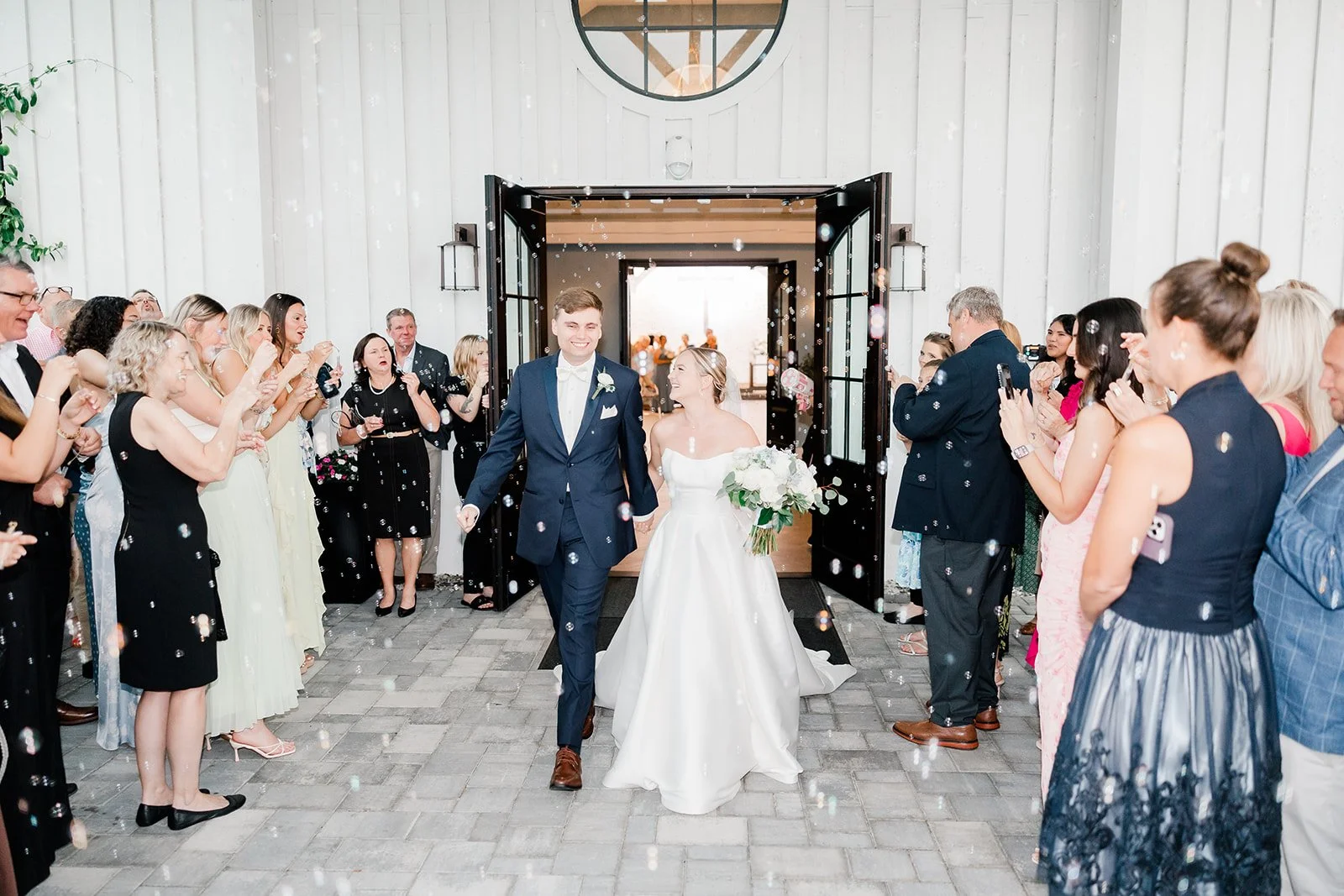 Bride and groom walking out of a wedding venue, surrounded by guests throwing confetti and taking photos.