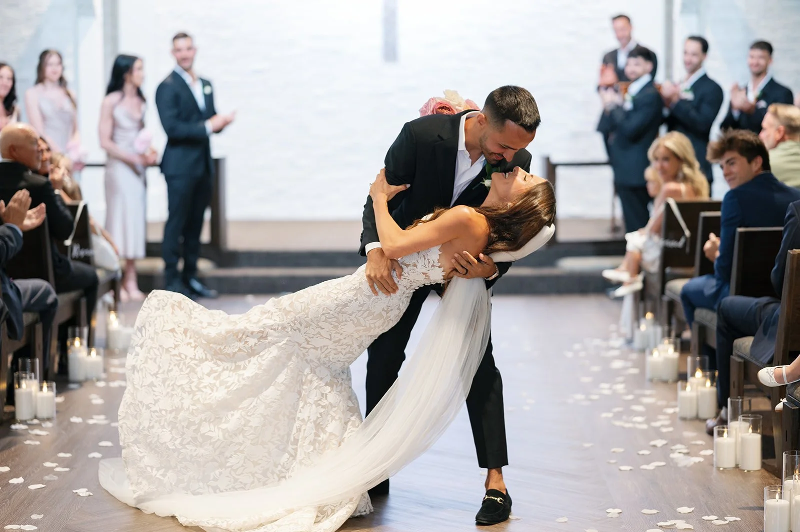 A bride and groom share a dance during their wedding ceremony in a decorated indoor venue with guests watching.