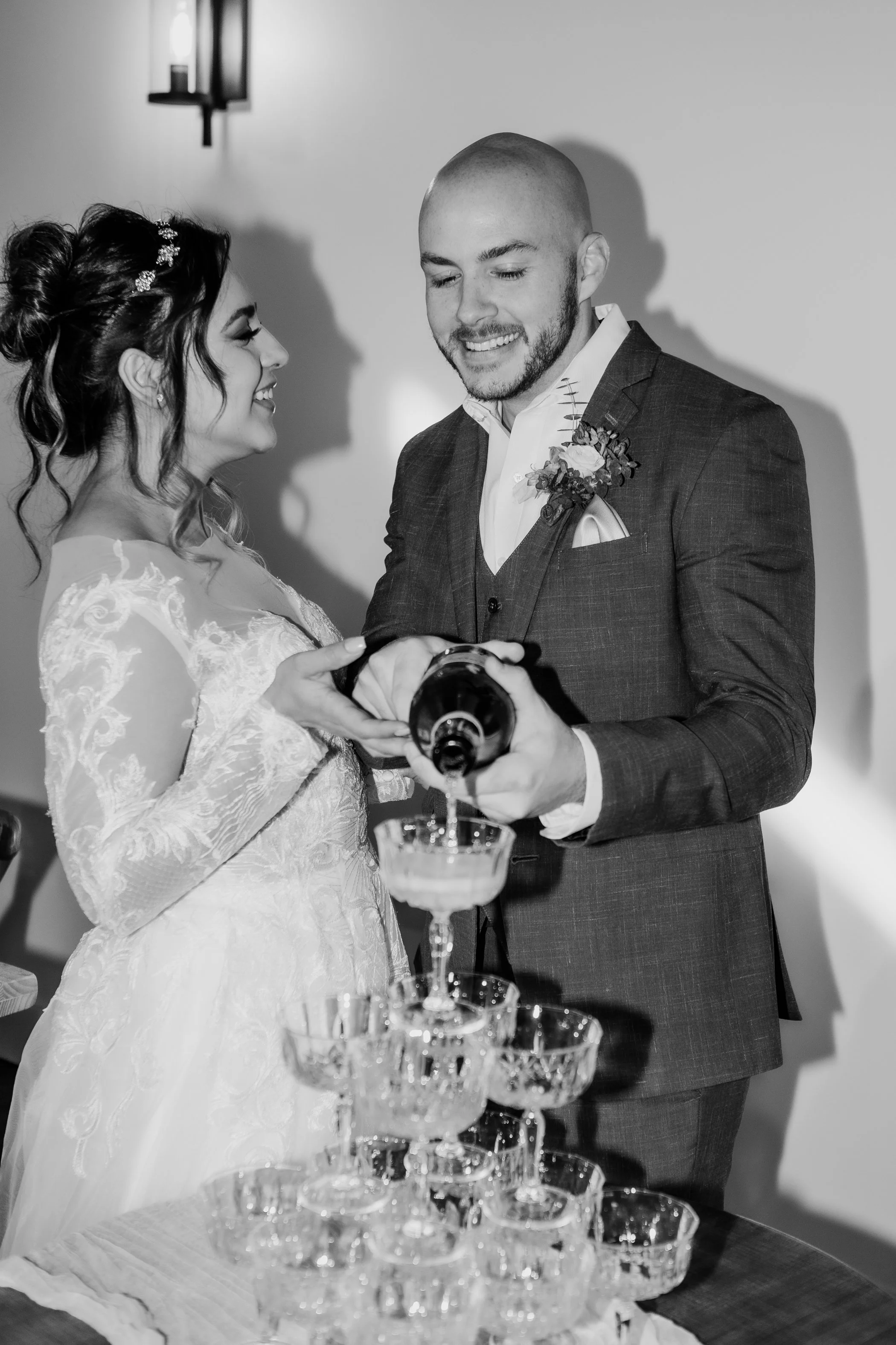 A bride and groom pouring champagne into a tower of glasses during their wedding celebration.