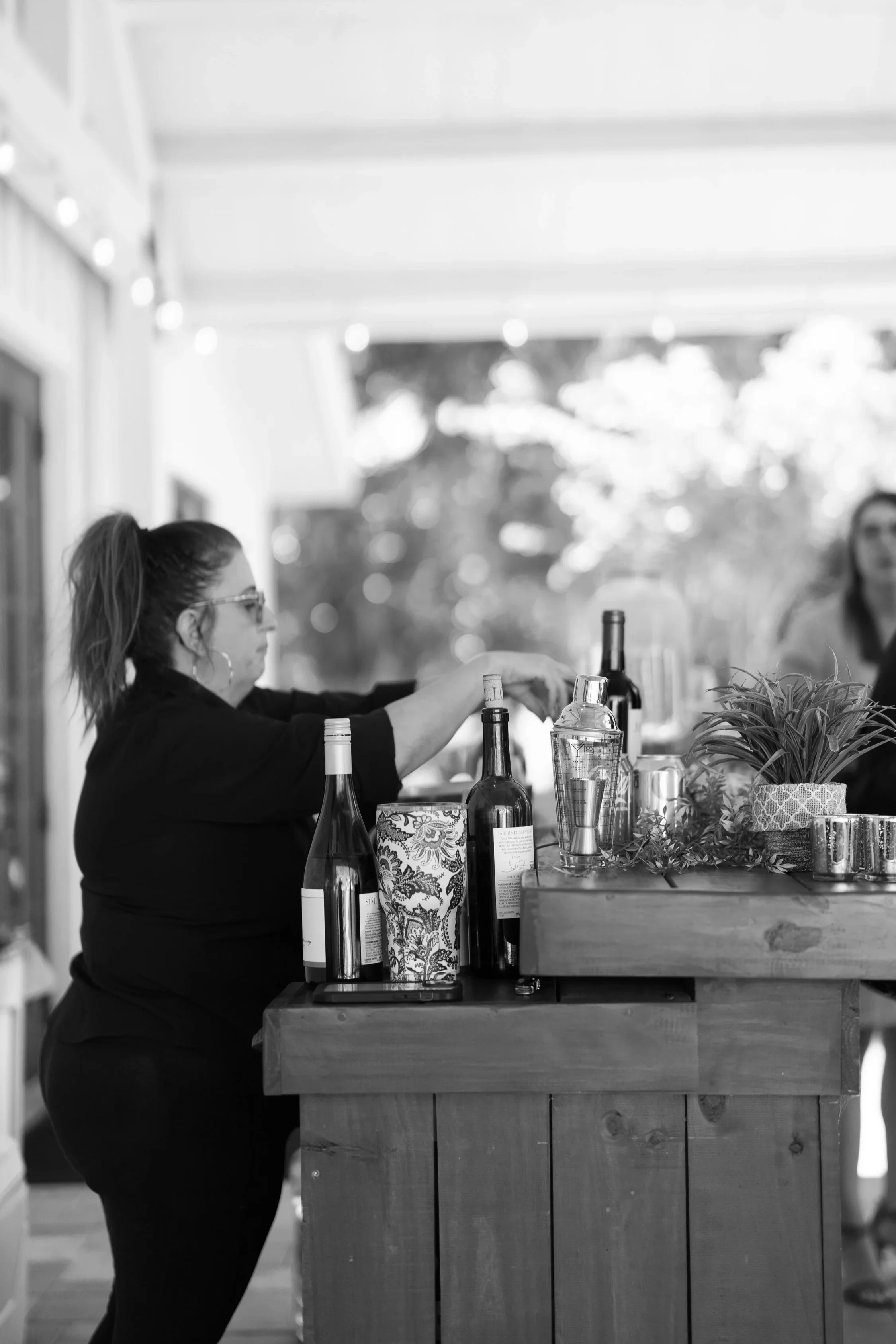 People gathering at a wine tasting event with bottles, glasses, and a large water pitcher on the table.