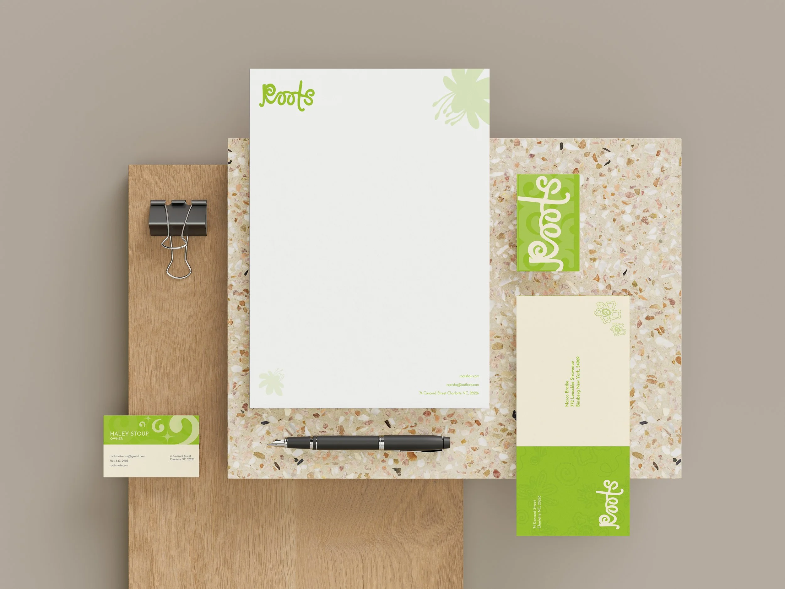 Corporate stationery set with papers, cards, and a pen on a speckled surface, featuring a green logo "Roots."