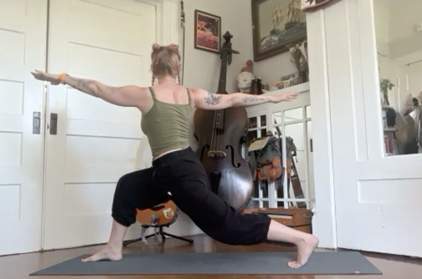 Woman practicing yoga in a lunge pose with arms extended in a home studio with musical instruments and artwork.
