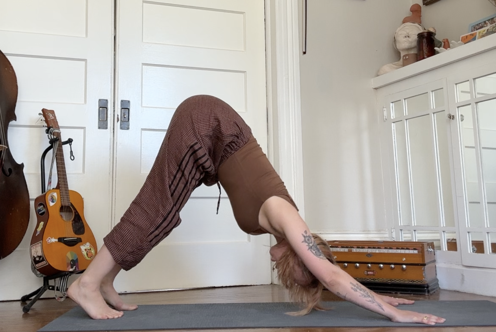 Person practicing yoga in downward dog pose on a mat in a room with guitars and musical instruments.