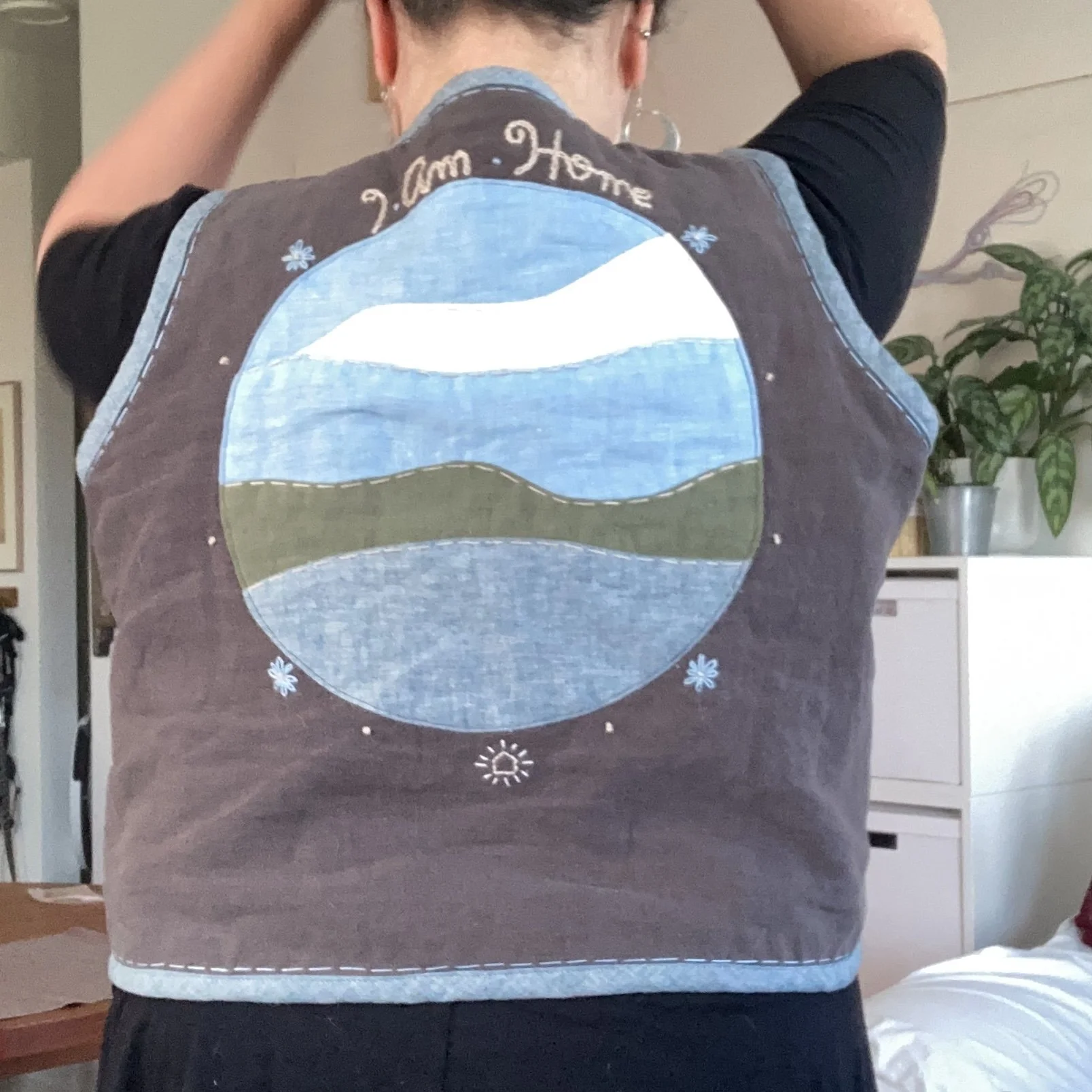 Person wearing a vest with a circular landscape design and the words "I am Home" at the top