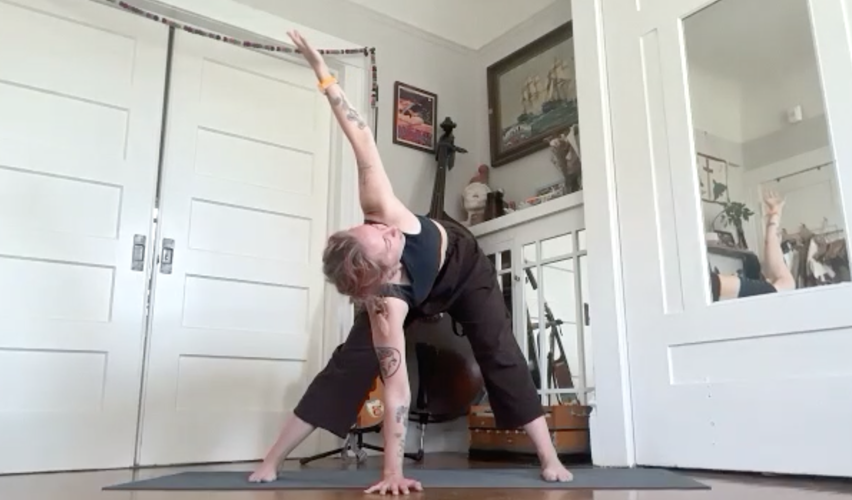 Person practicing yoga in a room, performing a downward dog pose with their left arm extended upward, transforming into a side plank, with a mirror reflecting their arm and pose.