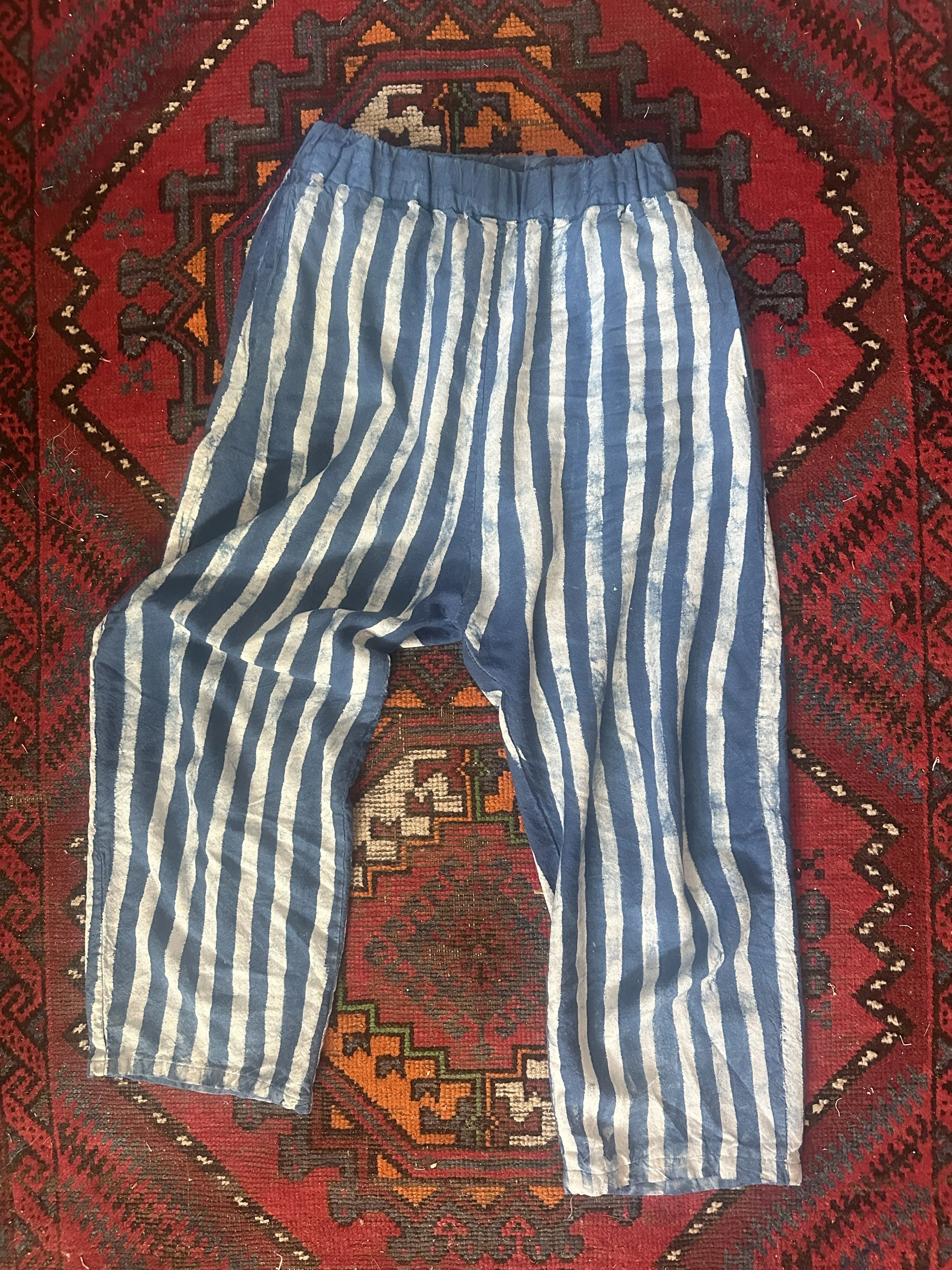 A pair of blue and white vertical striped pajama pants laid flat on a red patterned area rug.