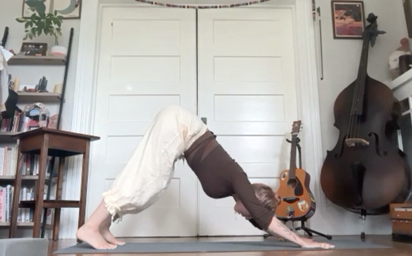 A person practicing yoga in a room with bookshelves and musical instruments, including a large double bass and an acoustic guitar, on the wall.