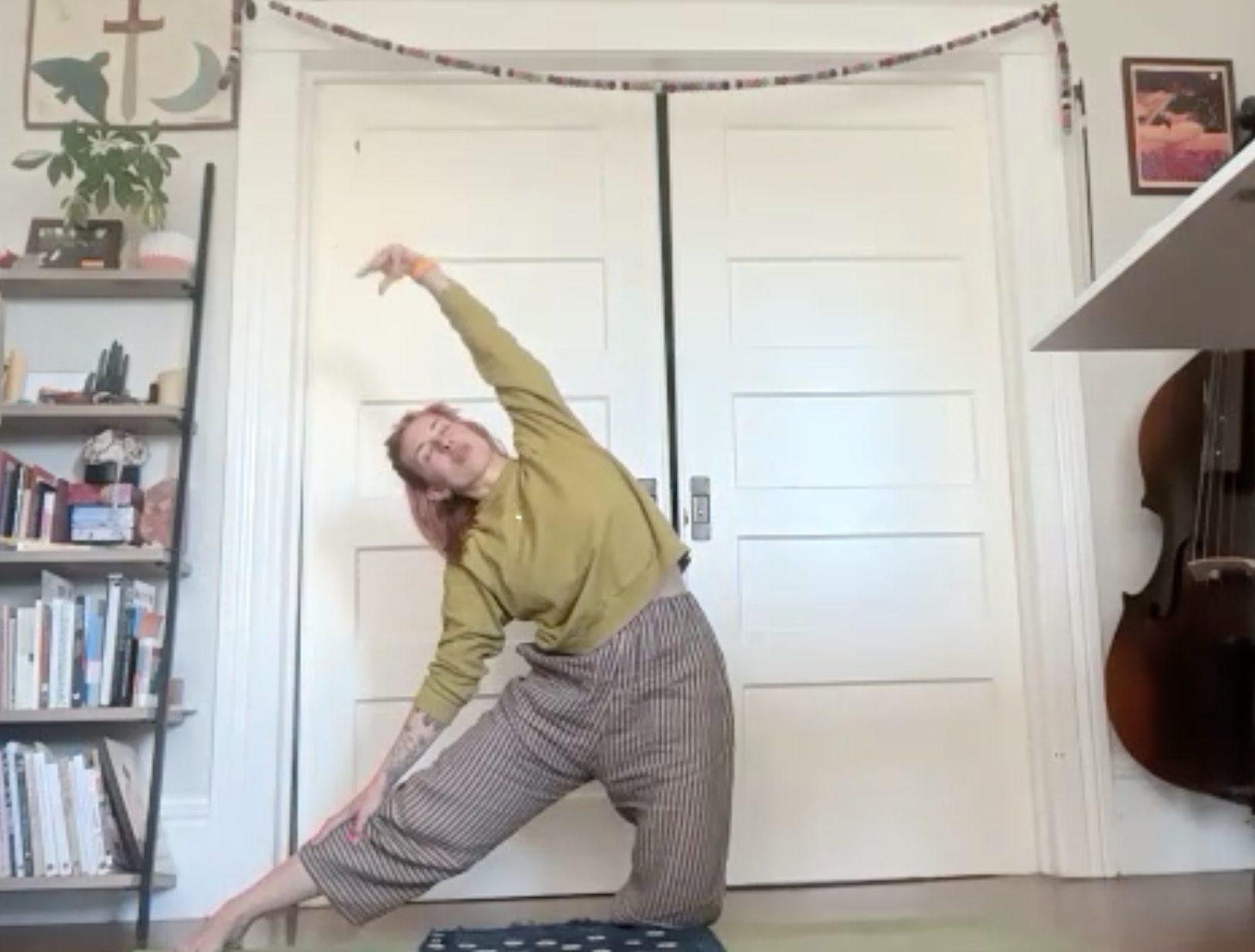 Person practicing yoga in a room with a bookshelf, framed pictures, and a guitar. The person is in a stretching pose.