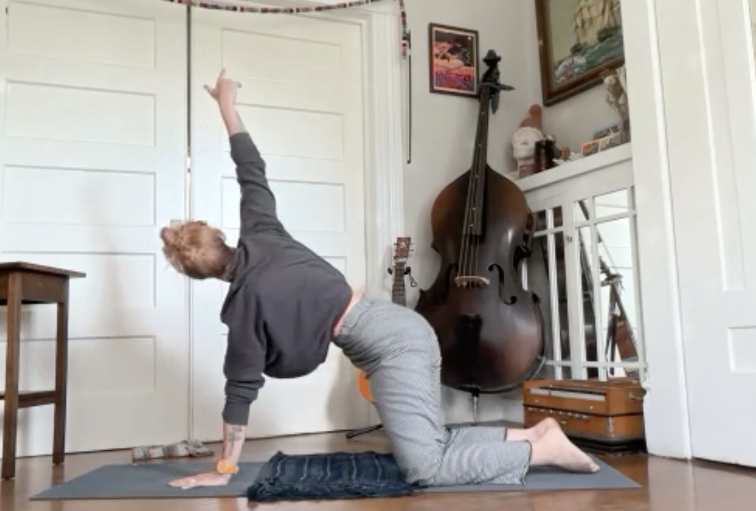 Person practicing yoga in a room with musical instruments, including a large double bass, guitar, and guitar case, on a yoga mat.
