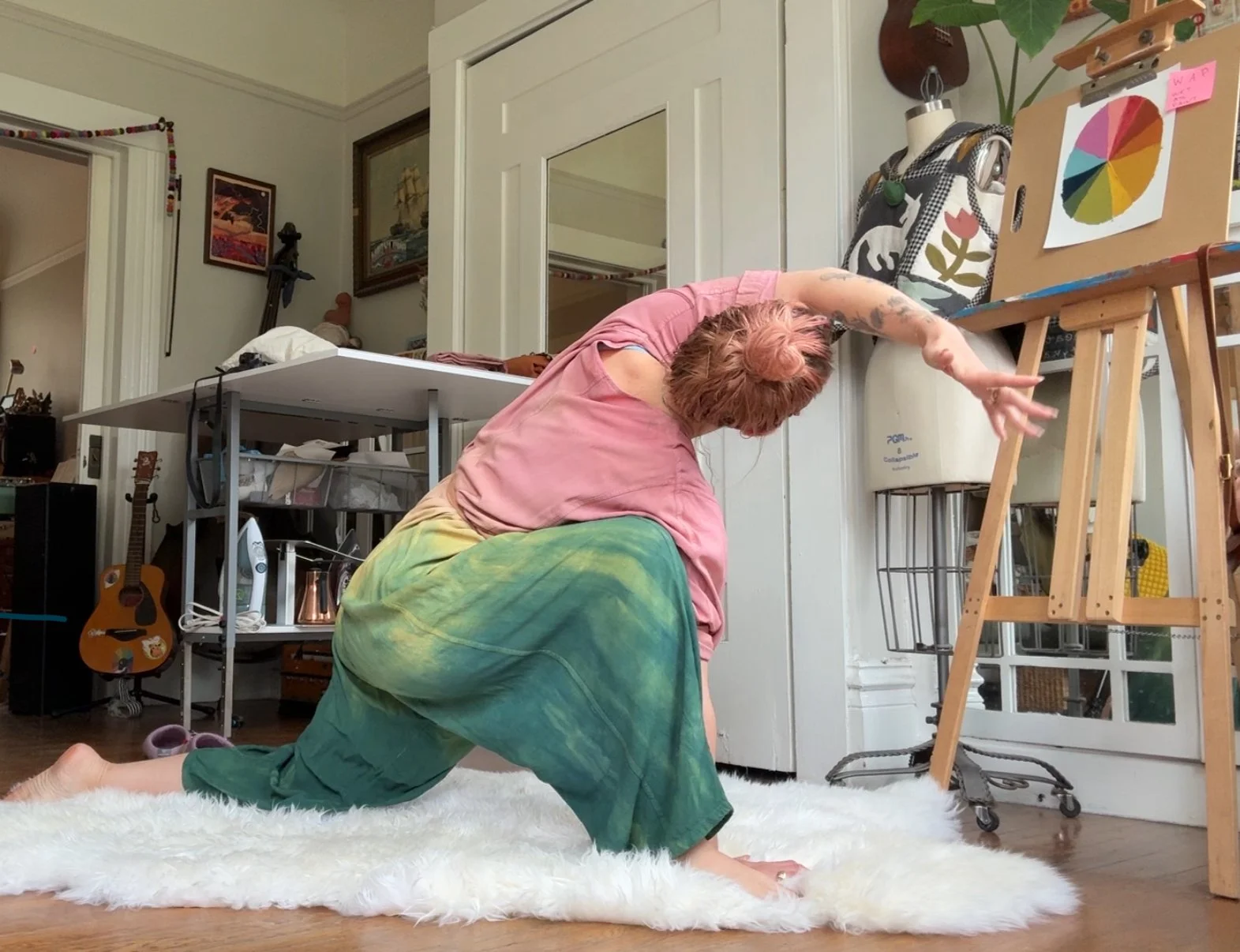 Person performing a yoga pose on a white rug in a room with musical instruments and artwork, reaching with their arm extended forward while kneeling on one knee.