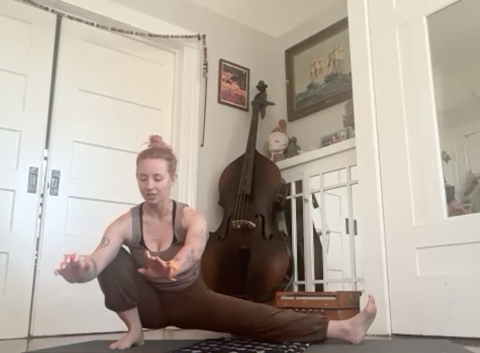 Woman practicing yoga in her living room, with a double bass and framed artwork on the wall behind her.
