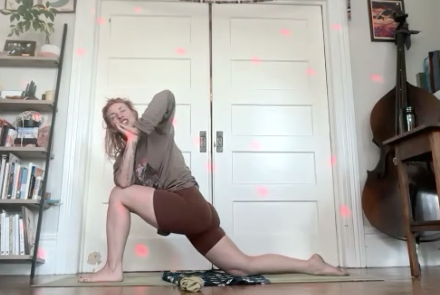 Person practicing yoga in a room with bookshelves and a double door, surrounded by pink lights or effects.