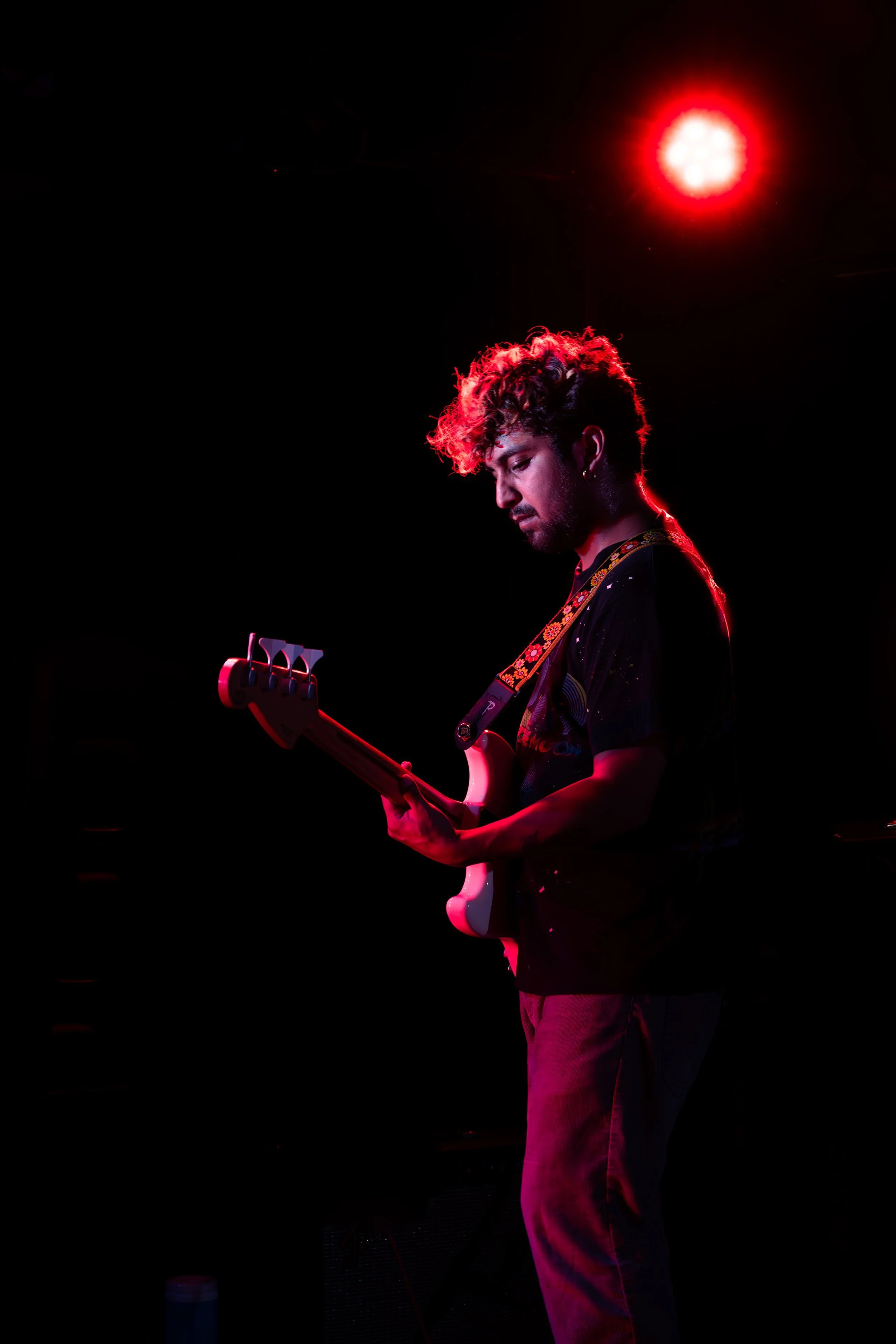 A musician with curly hair playing an electric guitar under red stage lighting