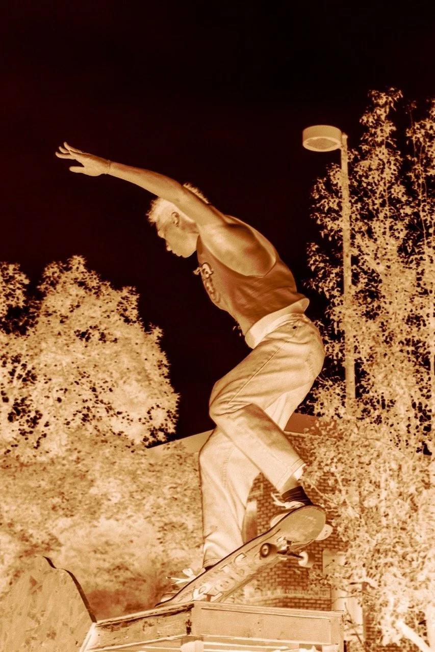 A skateboarder performing a trick on a ledge outdoors at night, with trees and a lamp post in the background.