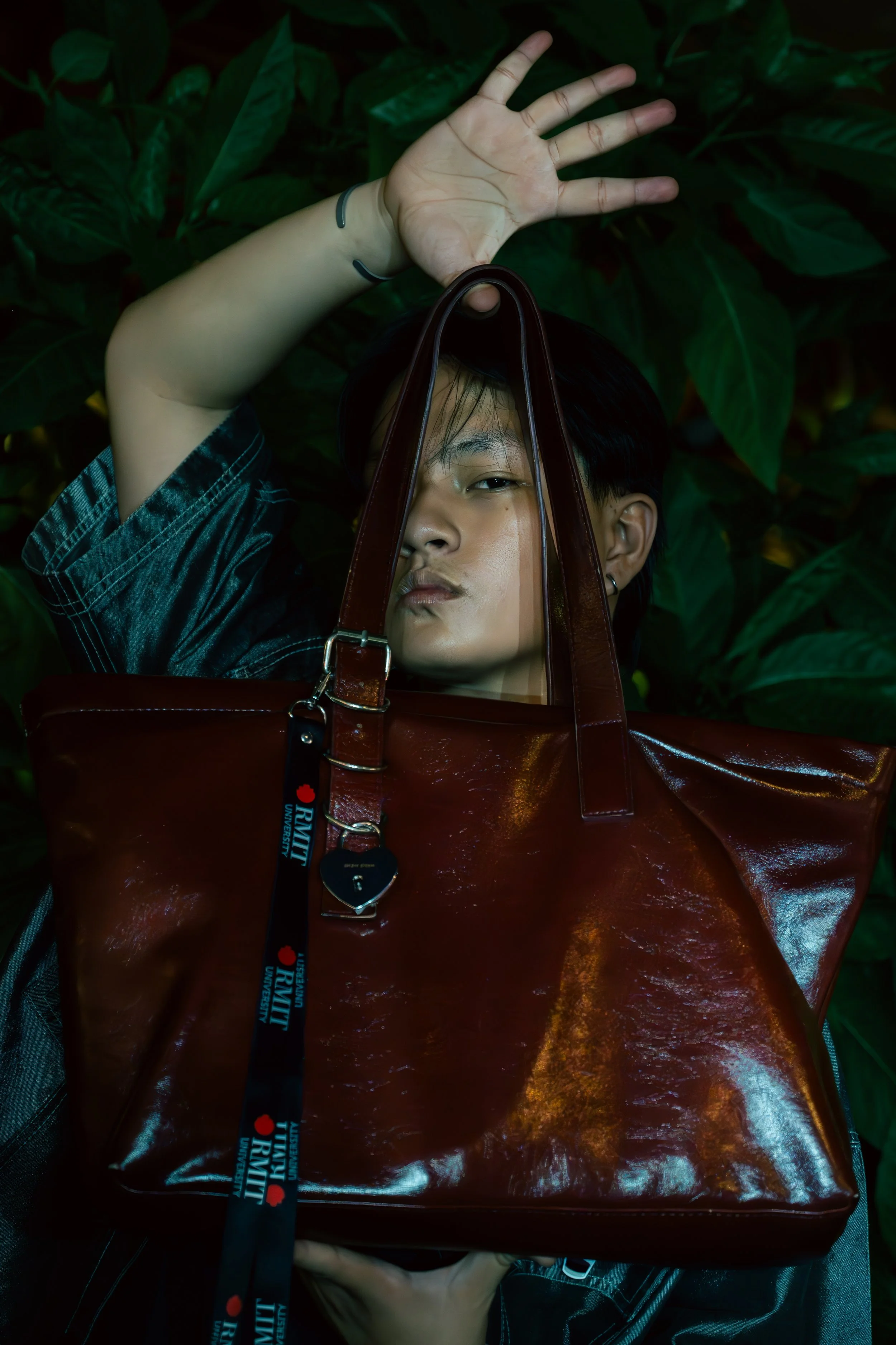 Person lying down with a large red bag covering their face, surrounded by green leaves.