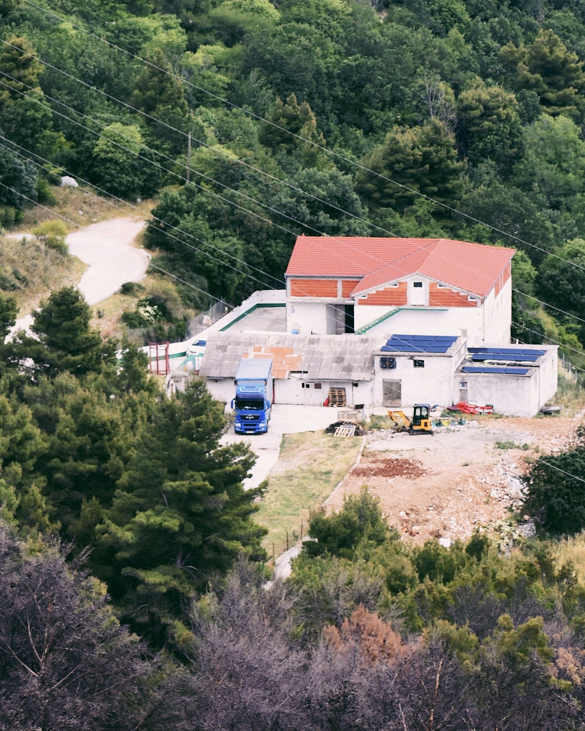 House under construction in a hilly, wooded area with construction equipment and vehicles nearby.
