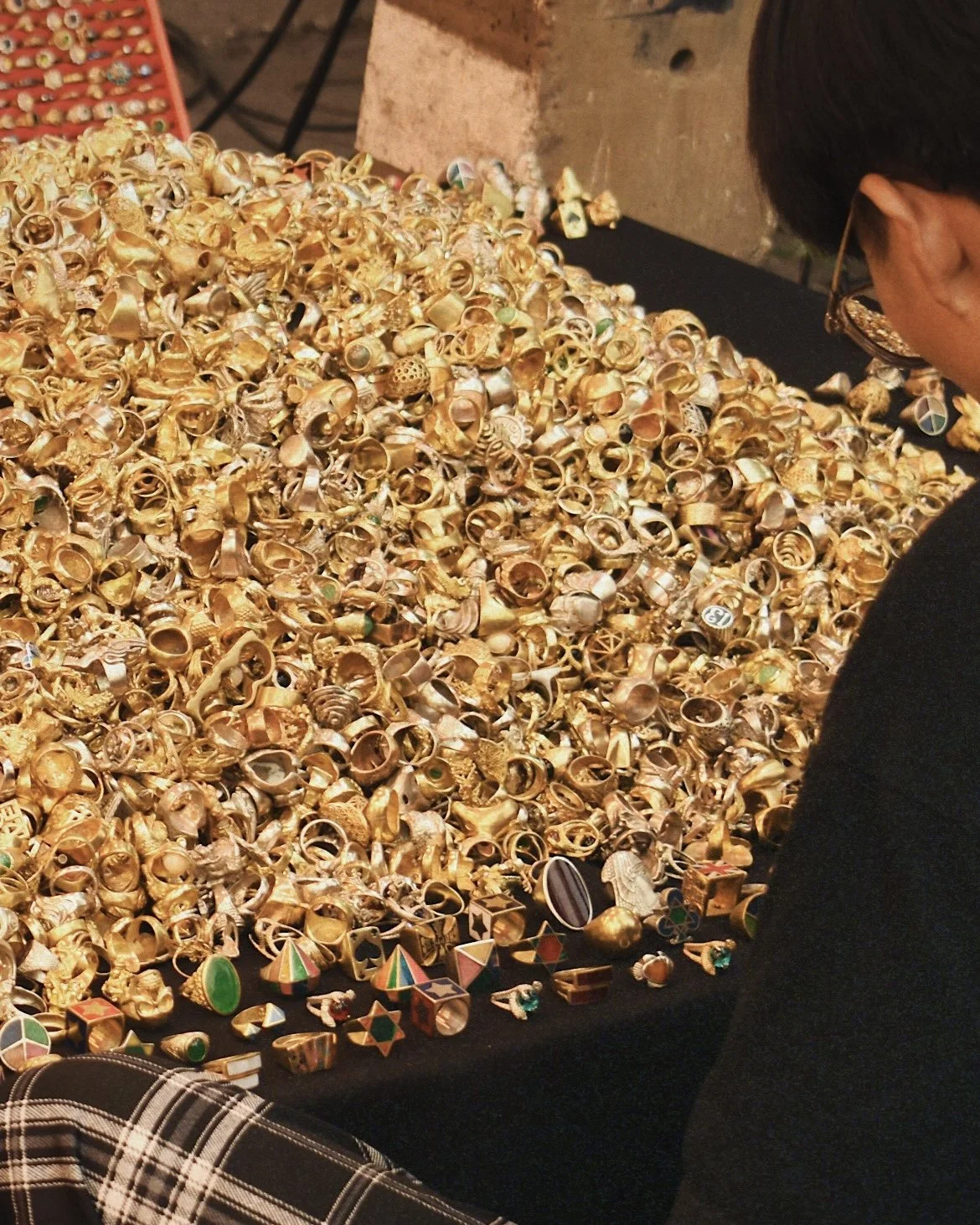 A person browsing a large pile of gold rings and jewelry at a marketplace or jewelry stand.