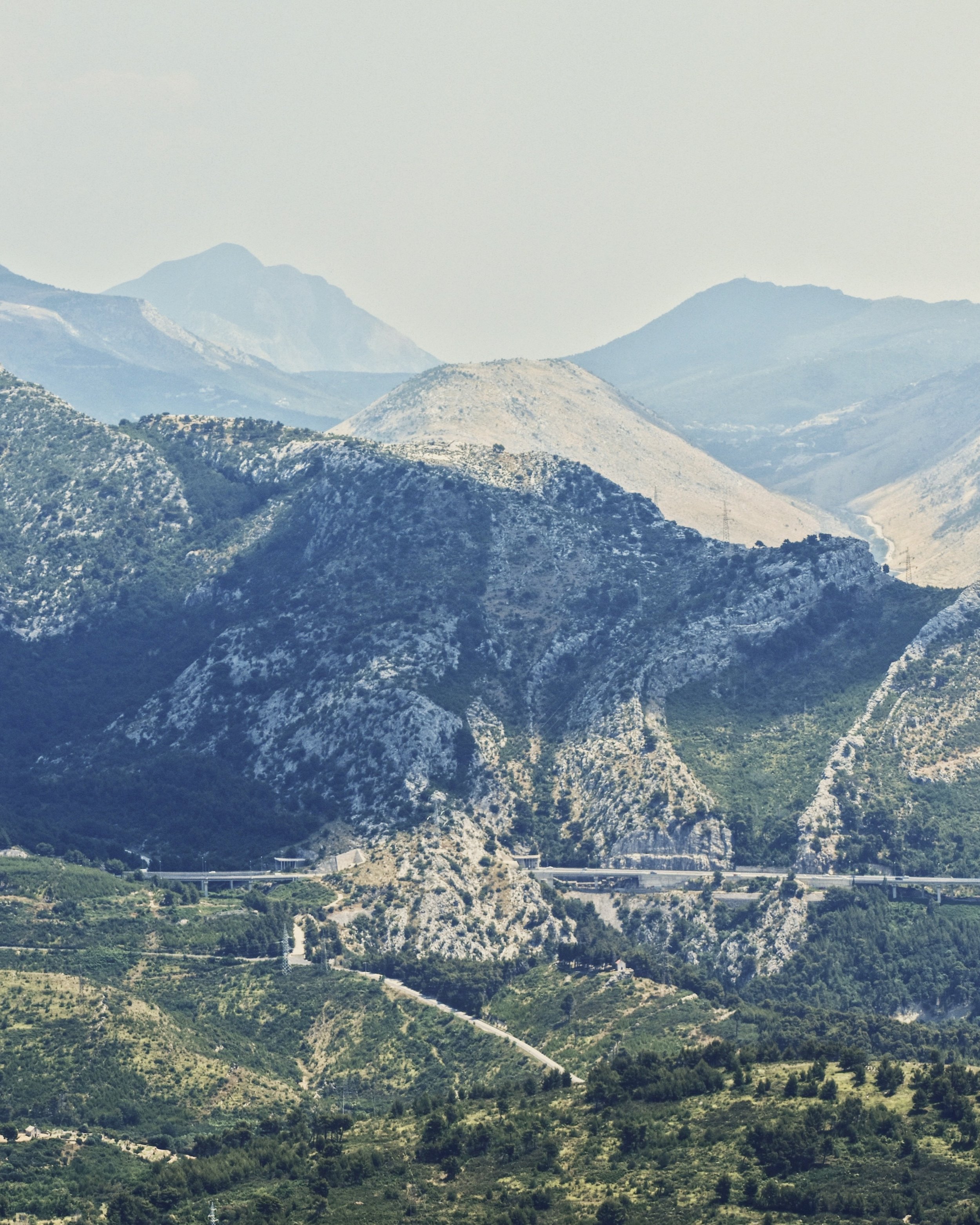 Mountain landscape with green valleys, rocky slopes, and distant peaks under a cloudy sky.