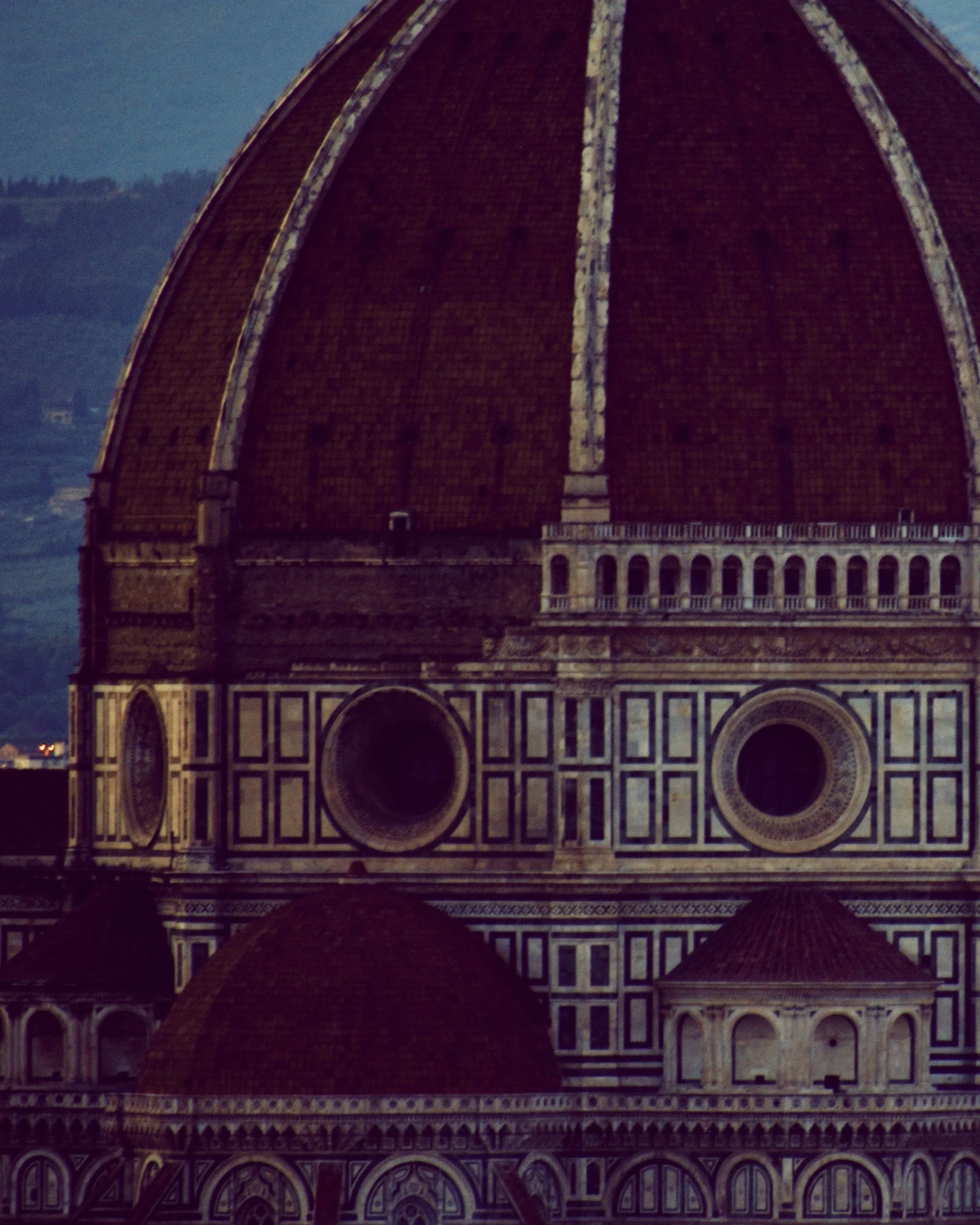 The image shows the top part of the Florence Cathedral's dome, with intricate patterned architecture and reddish-brown tiles, set against a darkening sky.