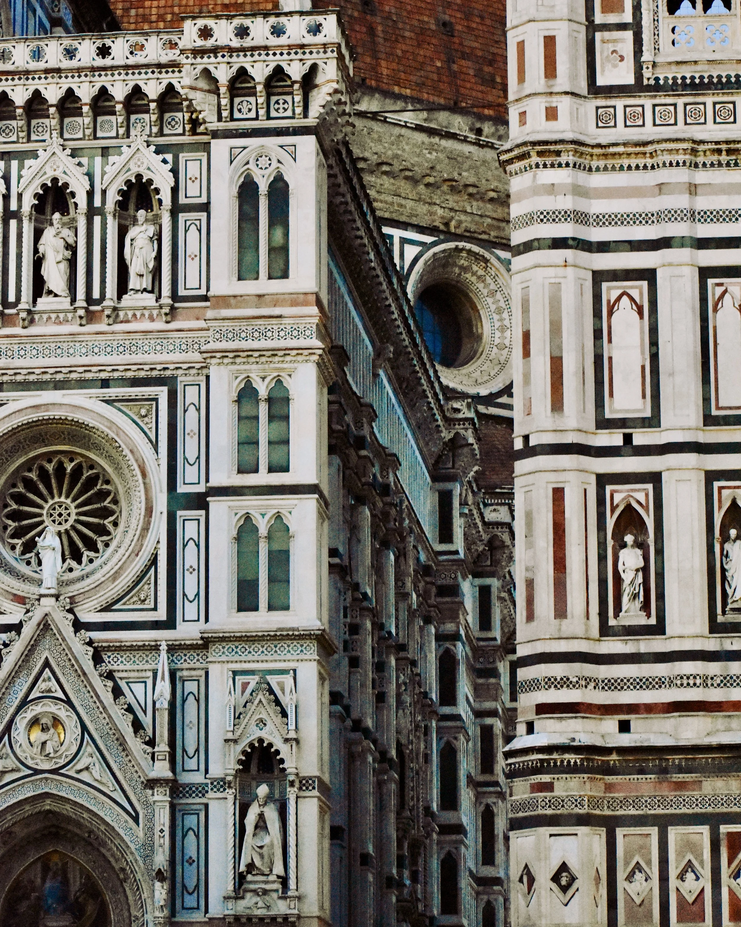 Close-up of the detailed facade of Florence Cathedral's exterior, showing ornate marble sculptures, stained glass windows, and intricate Gothic architectural features.