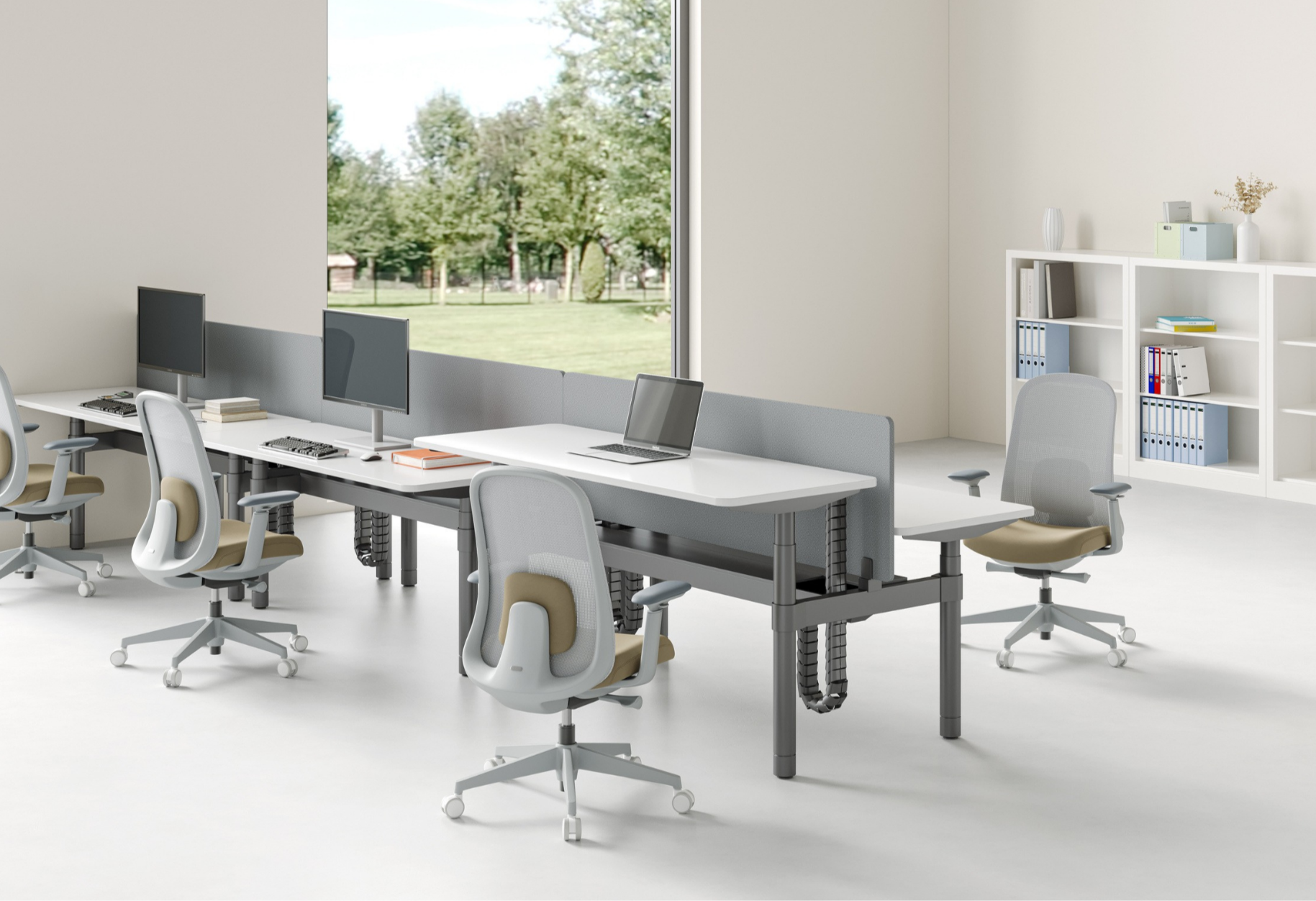 Modern office with white desks, beige and gray chairs, dual computer monitors, a laptop, and a large window showing a green park outside.