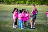 A female soccer coach giving instructions to young girls on a grassy field during a sports practice, all wearing pink shirts.