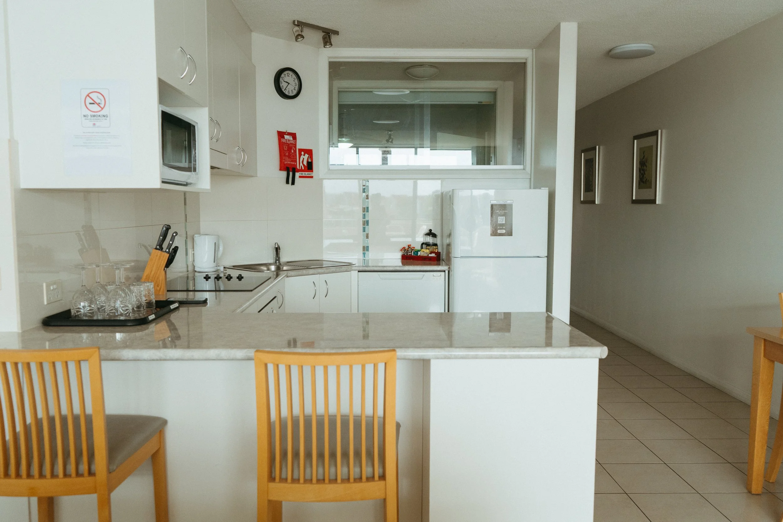 Lake Mulwala Yarrawonga - Empty kitchen with white cabinets, a small window, a white refrigerator, a microwave, a knife set, glasses, and wooden chairs.