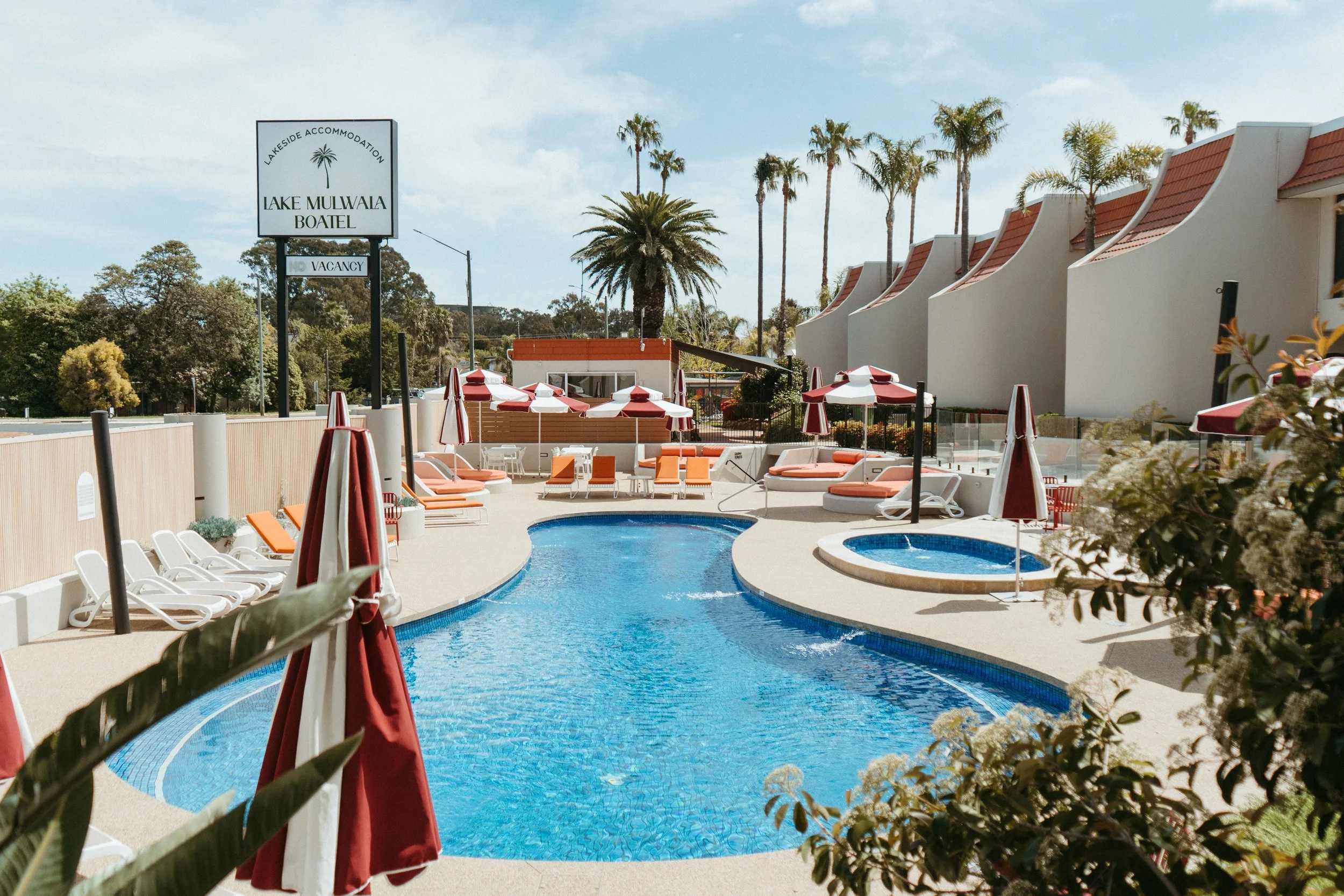 Lake Mulwala Yarrawonga - Swimming pool area with lounge chairs and umbrellas, surrounded by palm trees at a resort named Lake Mulwala Boatel.