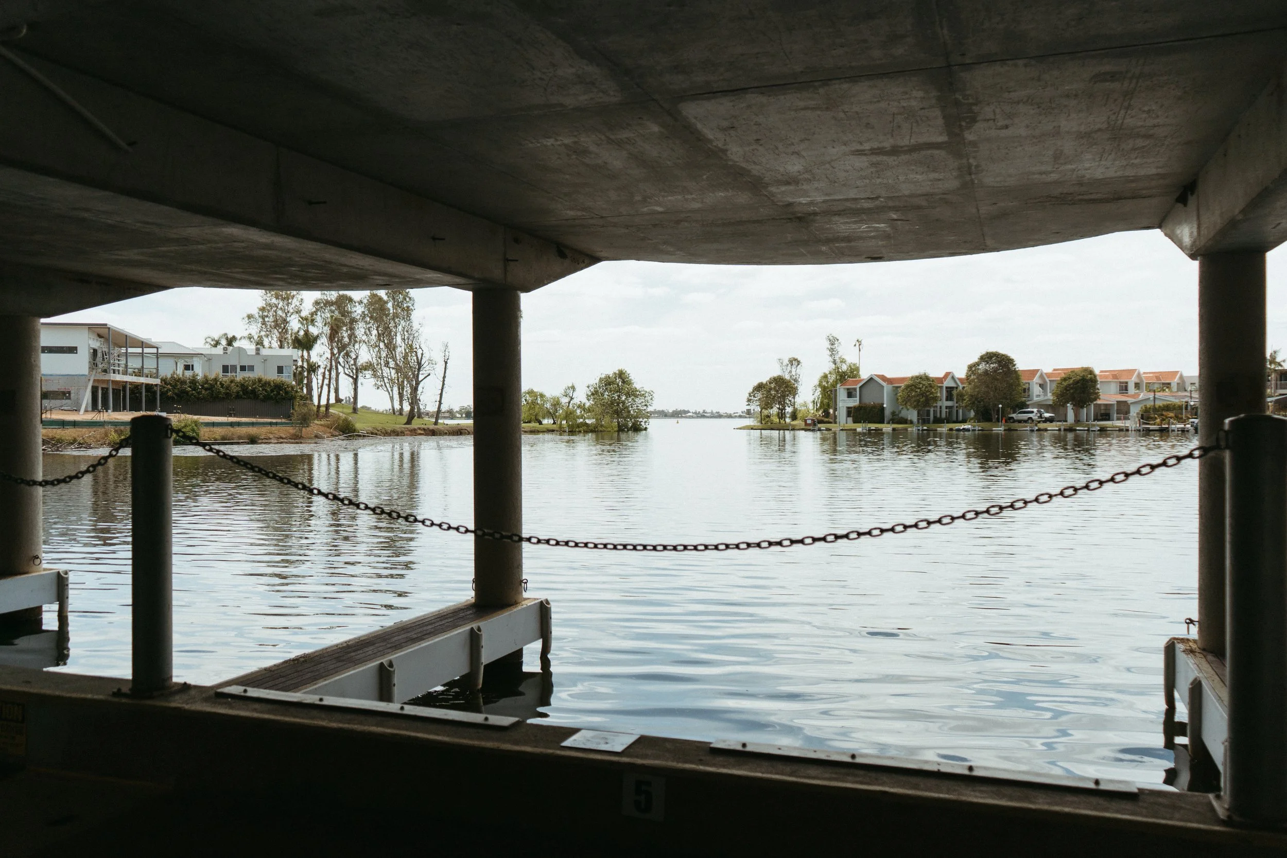 Lake Mulwala Yarrawonga - View of a body of water from under a concrete structure with residential buildings and trees on the opposite bank.