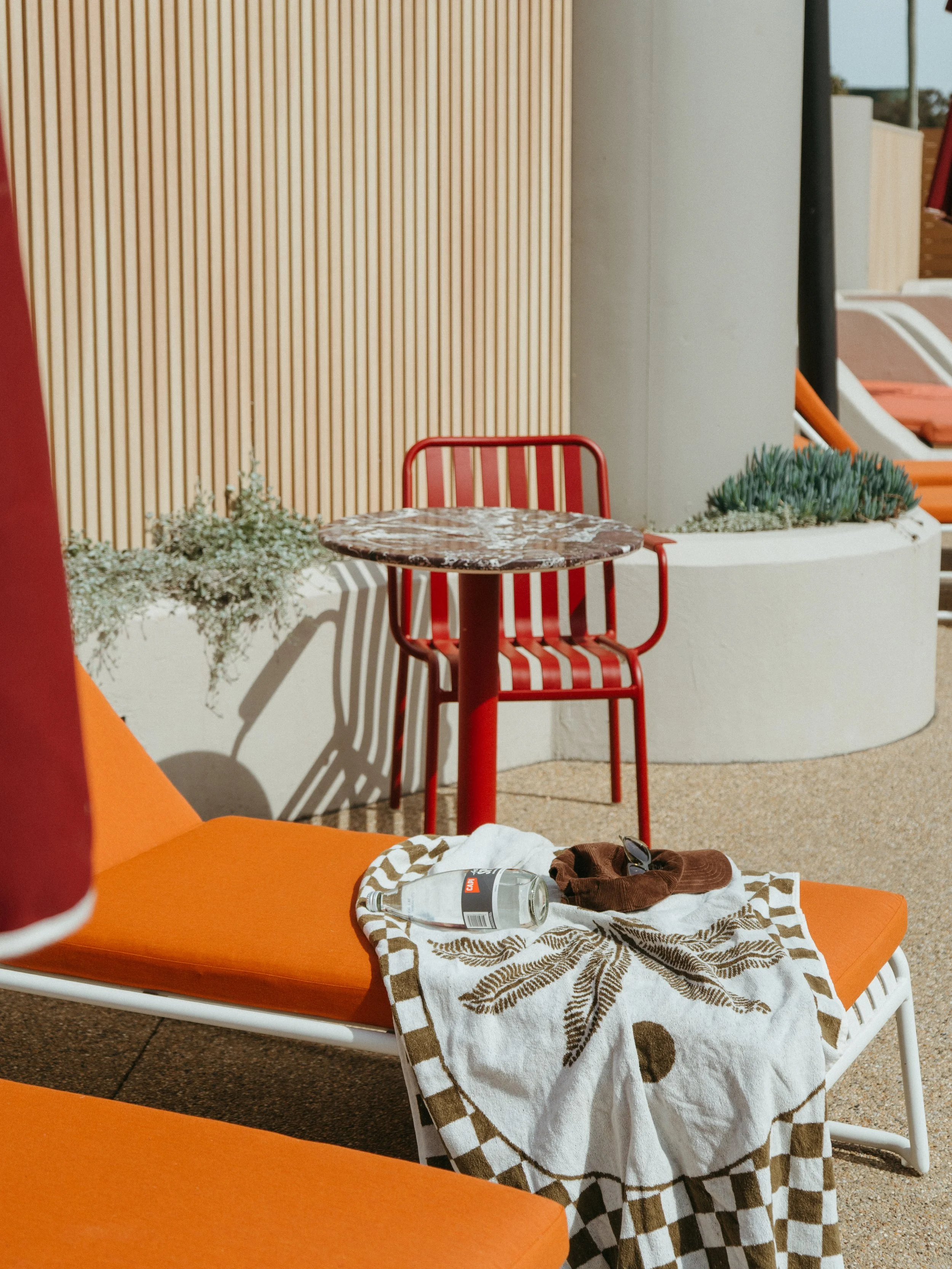 Lake Mulwala Yarrawonga - Outdoor scene with an orange lounge chair, a white towel with brown leaf pattern, sunglasses, and a water bottle on the towel. 