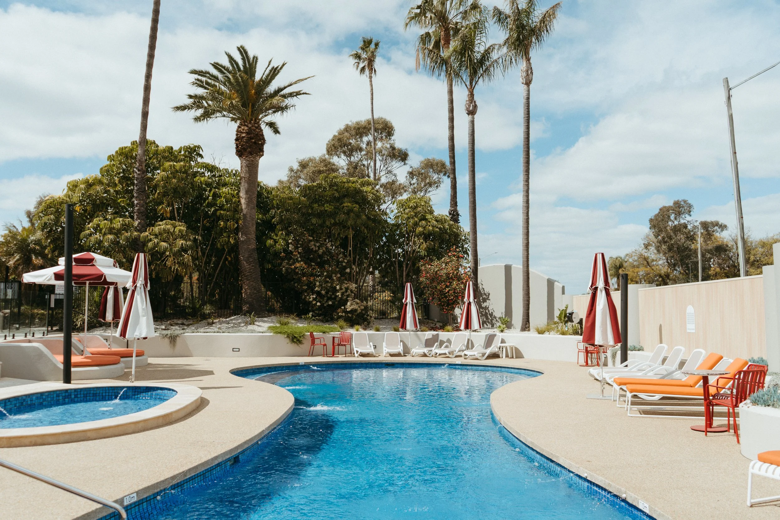 Lake Mulwala Yarrawonga - outdoor swimming pool area with lounge chairs, umbrellas, and tall palm trees on a sunny day.