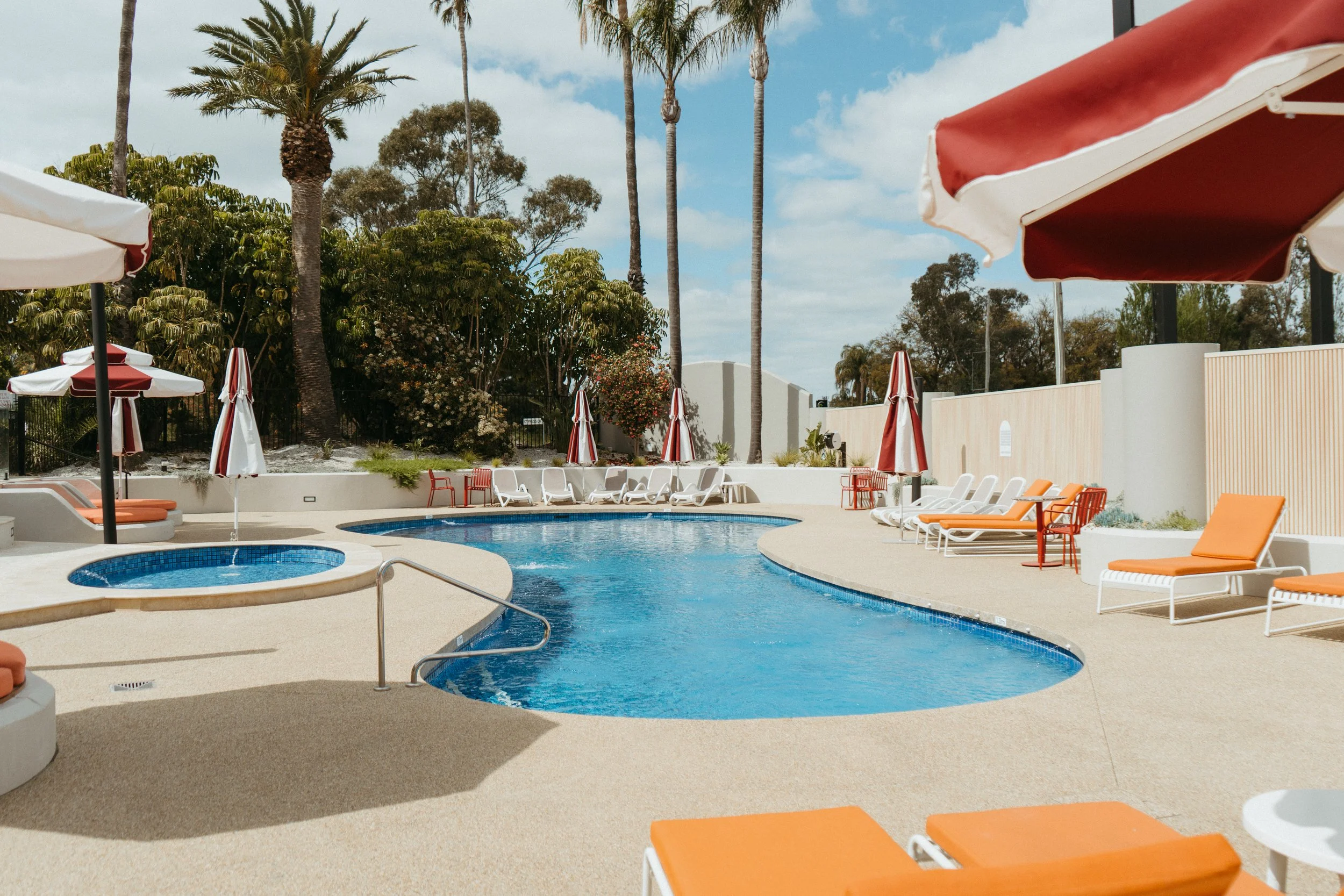 Lake Mulwala Yarrawonga - swimming pool area with lounge chairs and umbrellas, surrounded by trees under a partly cloudy sky.