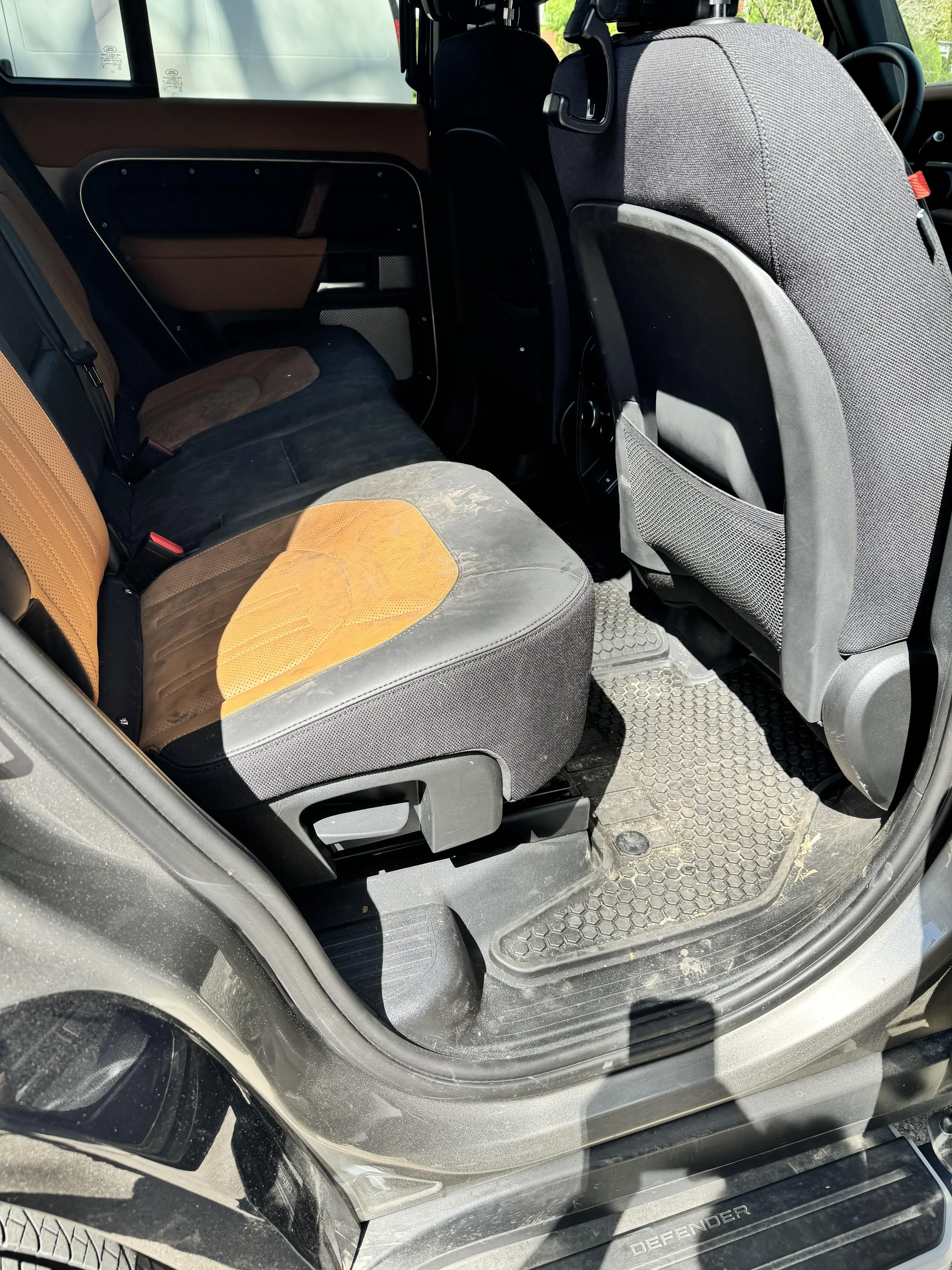 Rear seat interior of a car with two-tone upholstery, showing a rubber floor mat and car door frame.