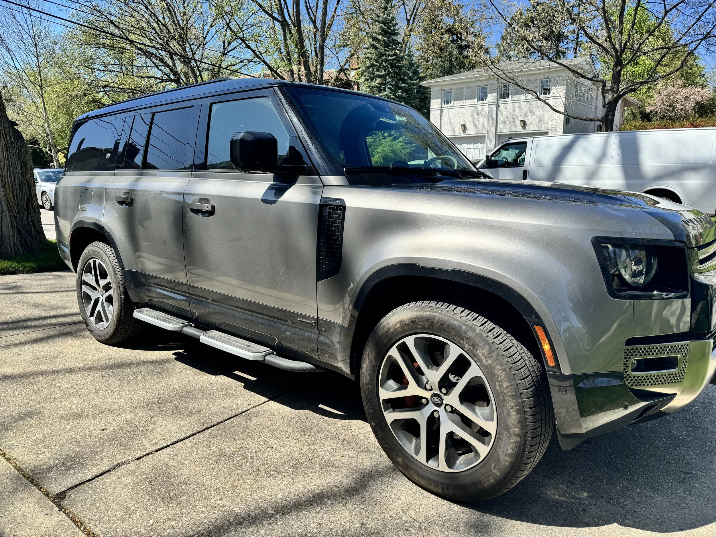 Gray SUV parked on driveway, surrounded by trees and residential buildings, under a clear blue sky.