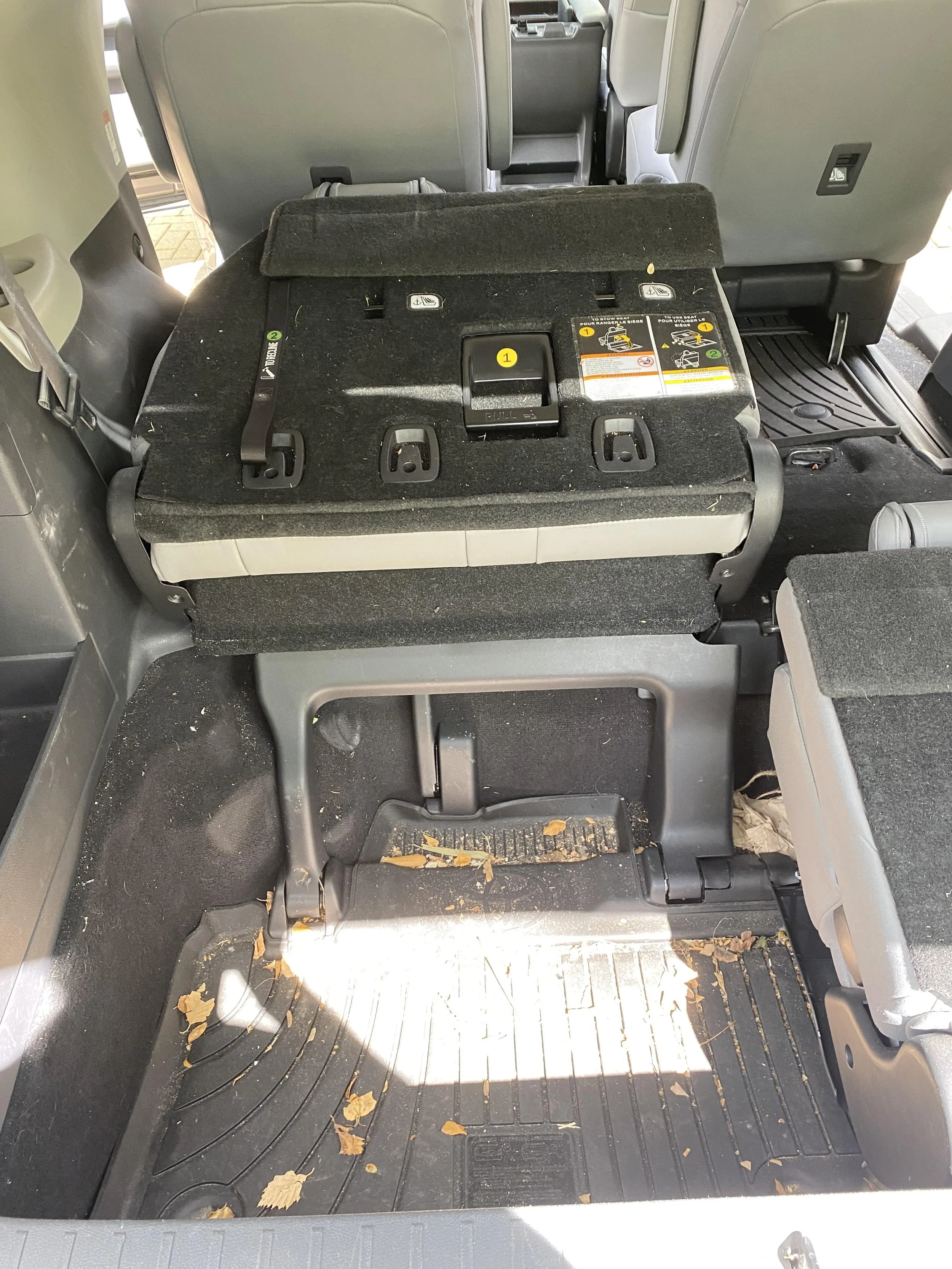 Interior of a car showing folded rear seats and trunk space, with some debris on the floor mat.
