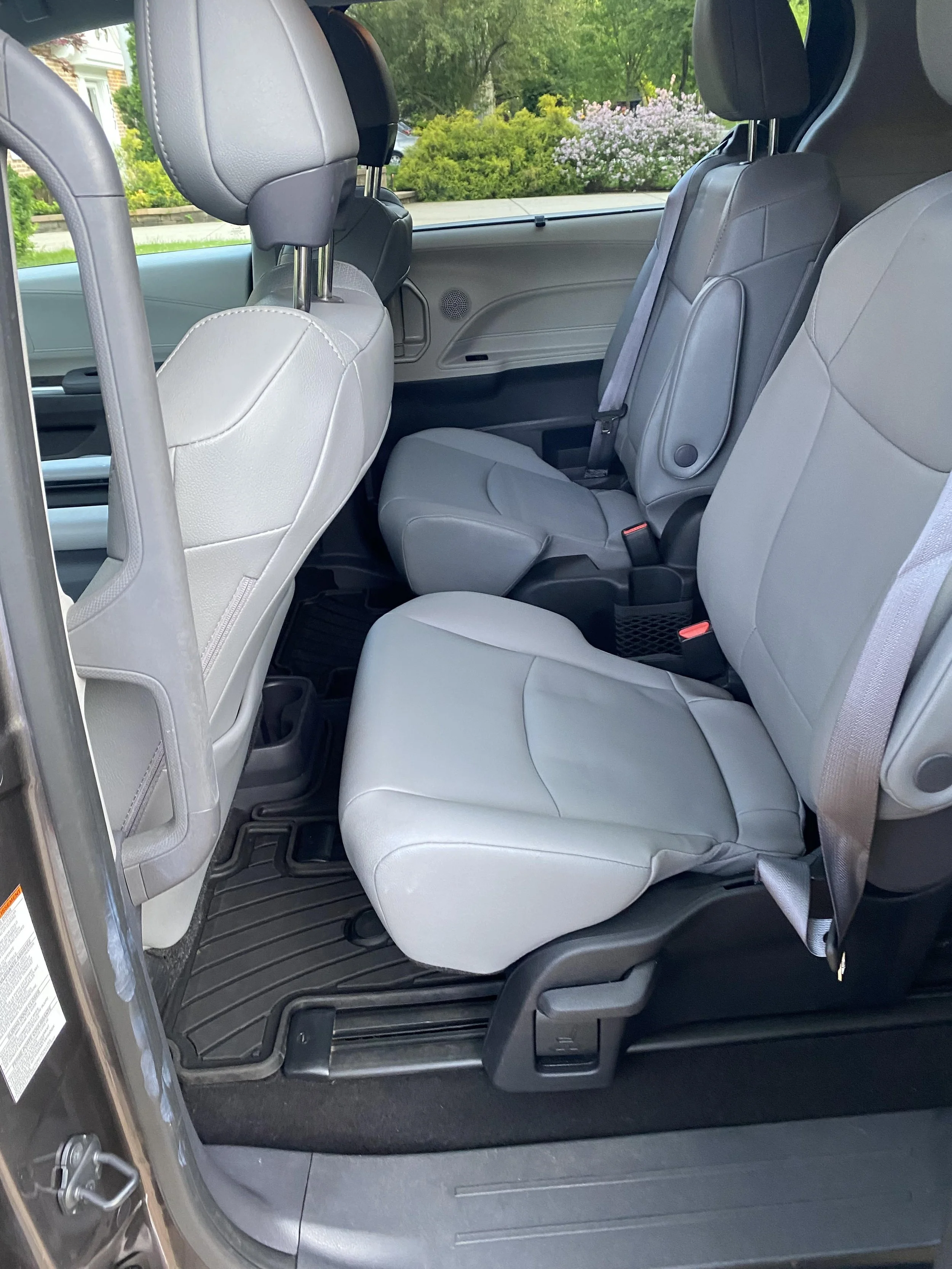 Interior of a vehicle showing two gray leather seats in a back row with a dark floor mat.