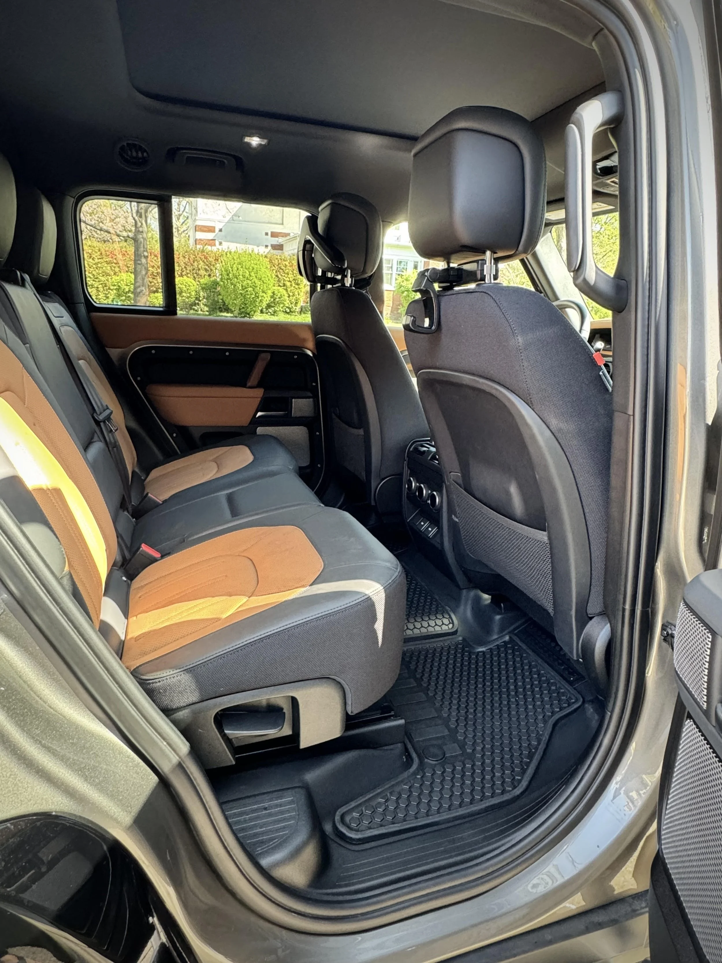Interior of a vehicle showing back seats with brown and black upholstery, rubber floor mats, and rear side vents.