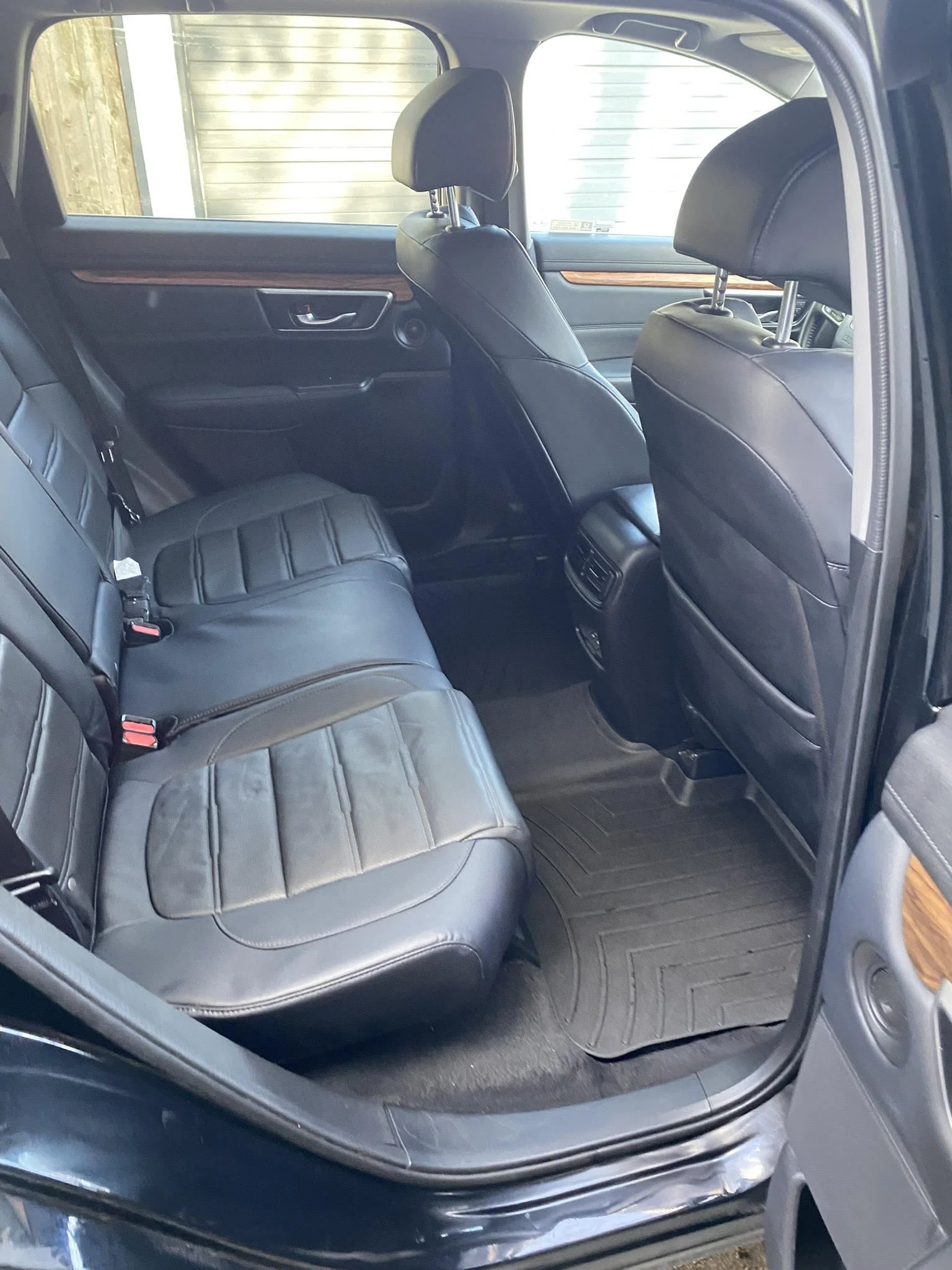 Interior of a car showing black leather back seats with wooden trim and rubber floor mats.