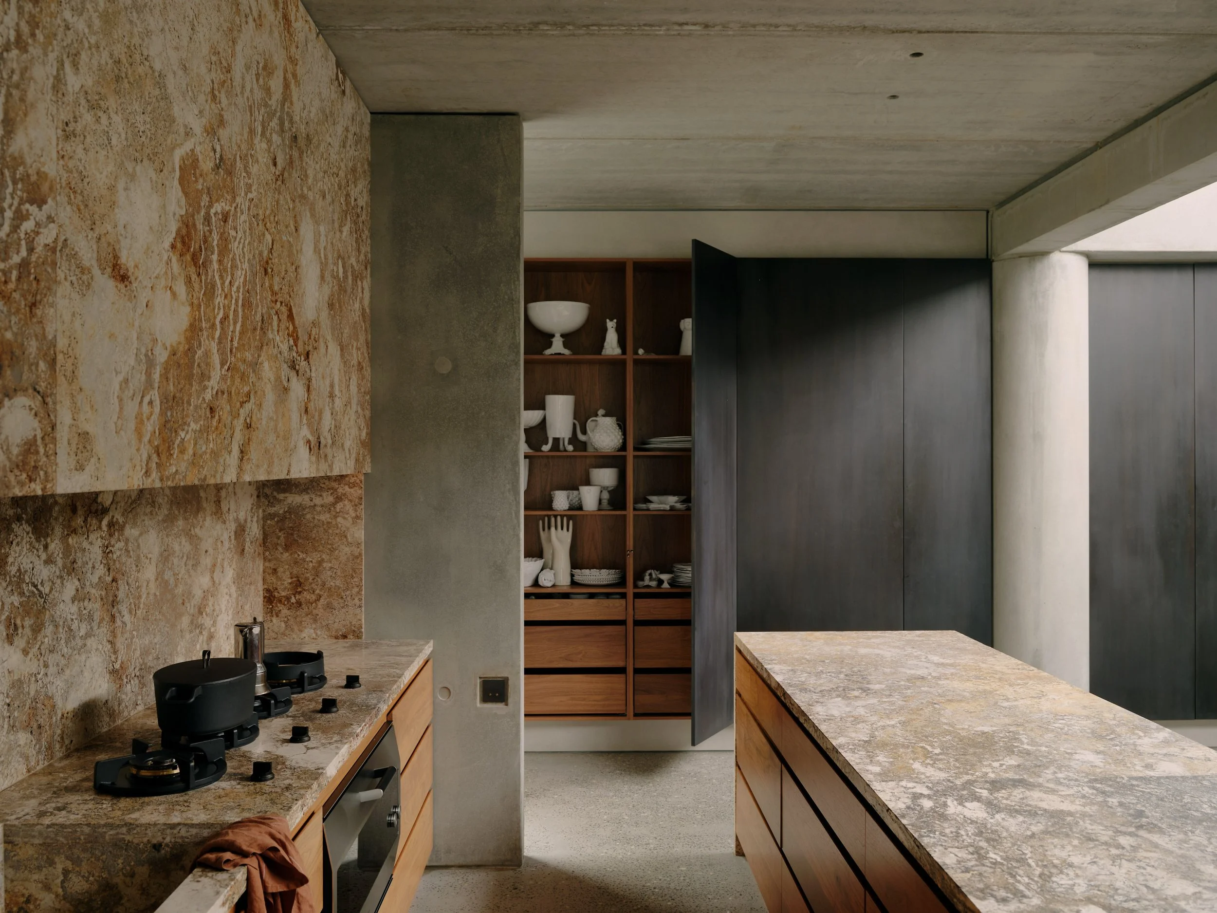 Subtle, modern kitchen with Walnut cabinetry, Travertine benchtop and splashback. A nod to the warm earthy tones and textures. Positioned against the exposed raw concrete structure.