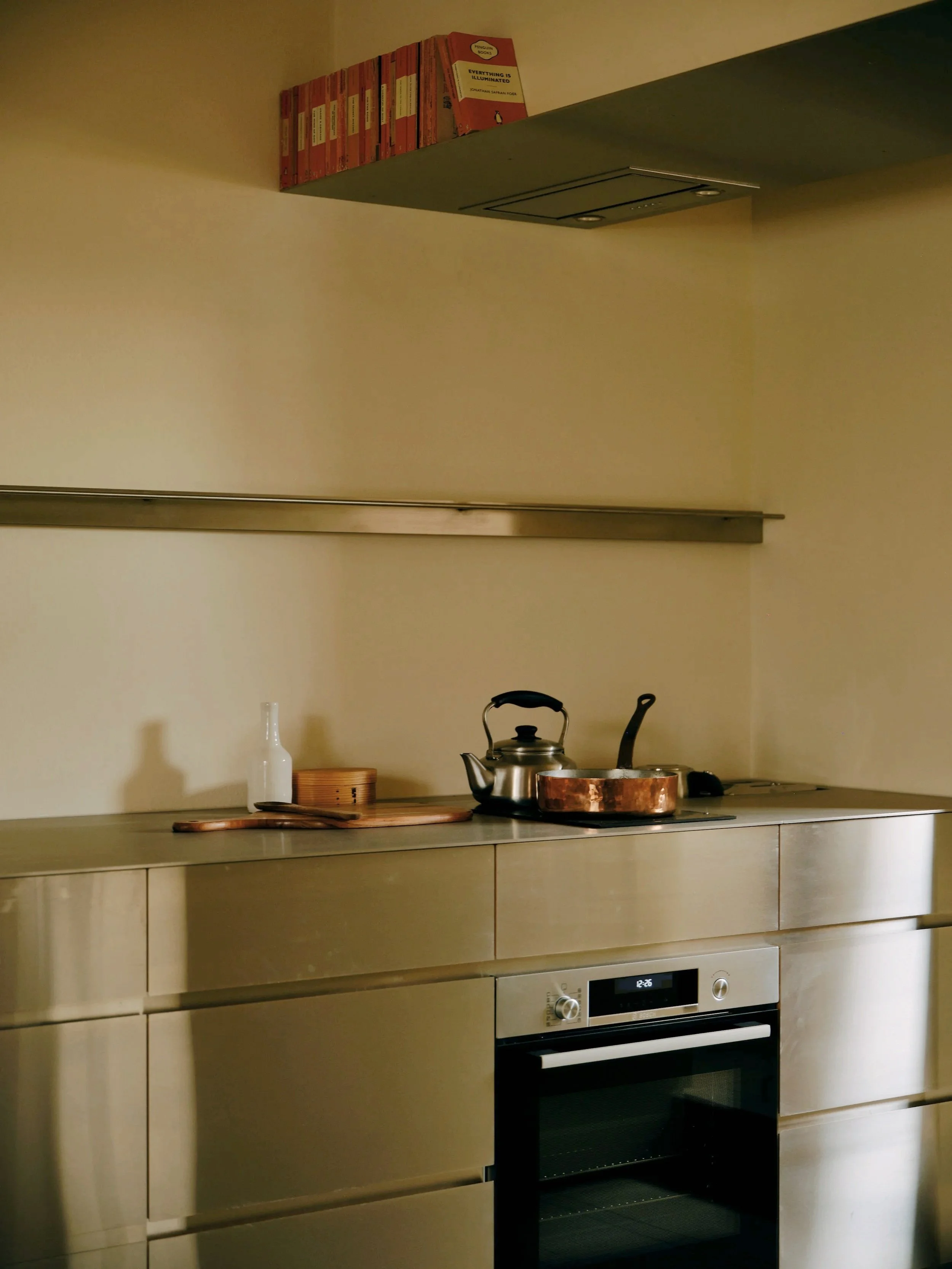 Custom Stainless Steel fabrication creating sharp, clean, defined lines for this apartment kitchen. Integration of the rangehood into the bookshelf highlights the minimal design, yet maximised usable space and storage.
